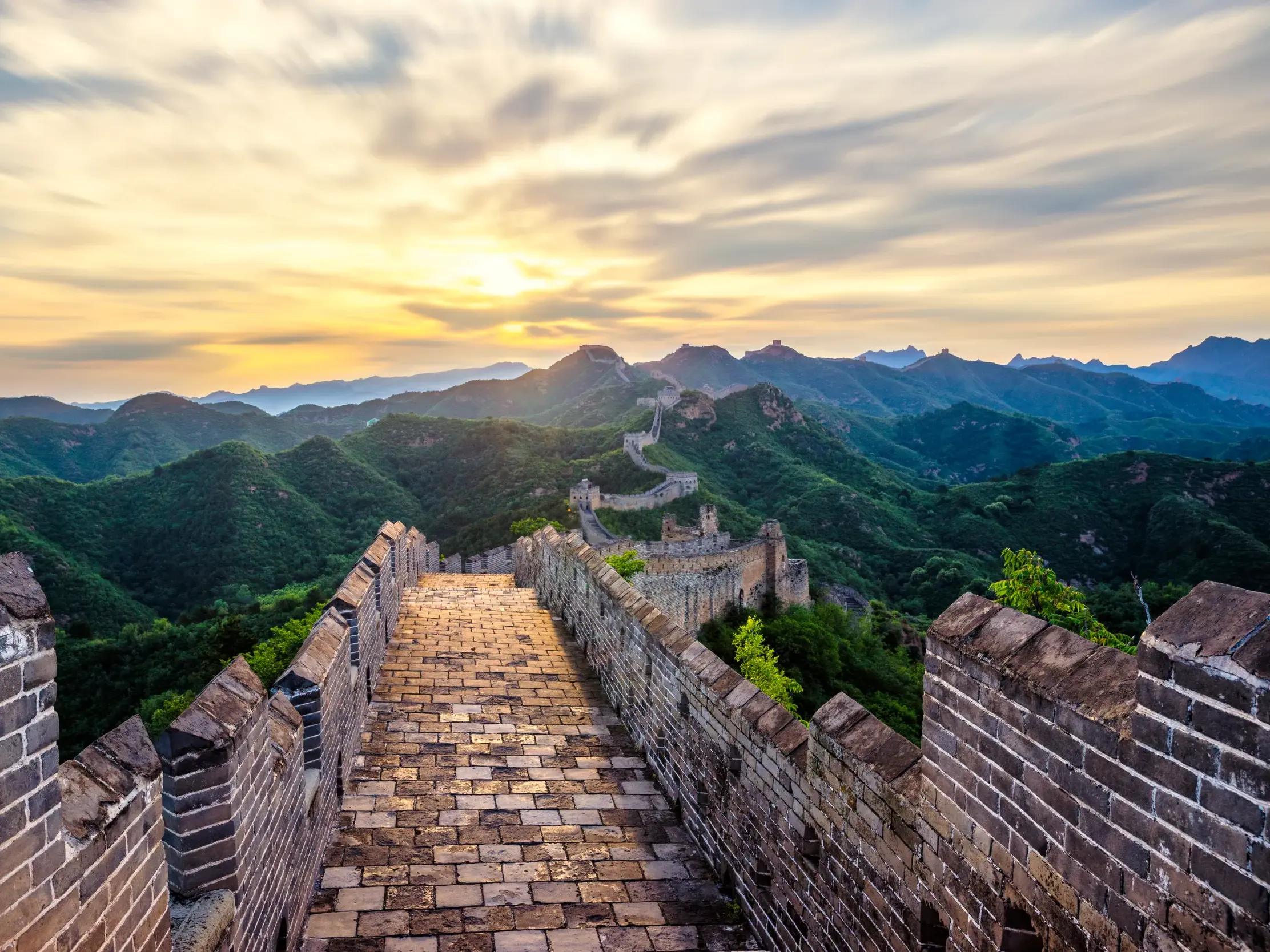 Die Große Mauer in China, ein UNESCO-Welterbe, schlängelt sich bei Sonnenaufgang über eine weite grüne Berglandschaft.