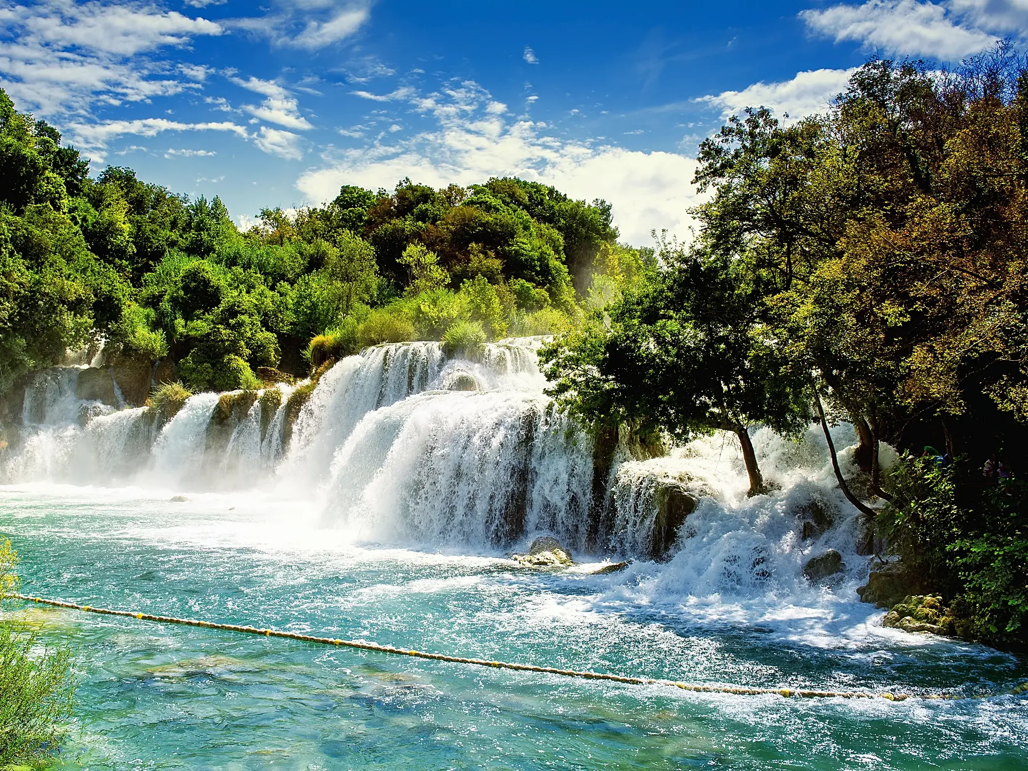 Breite, stufenförmige Wasserfälle im Krka-Nationalpark in Kroatien stürzen in türkises Wasser, umgeben von dichten Wäldern.