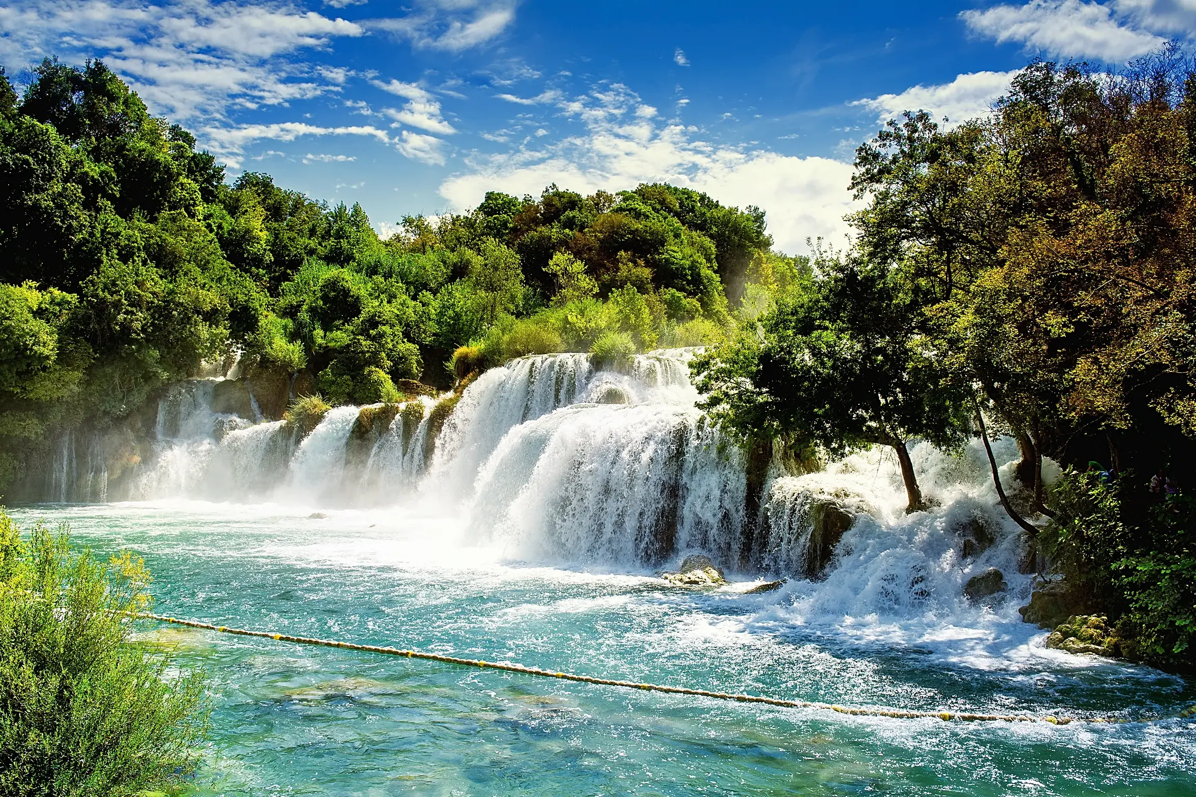 Breite, stufenförmige Wasserfälle im Krka-Nationalpark in Kroatien stürzen in türkises Wasser, umgeben von dichten Wäldern.