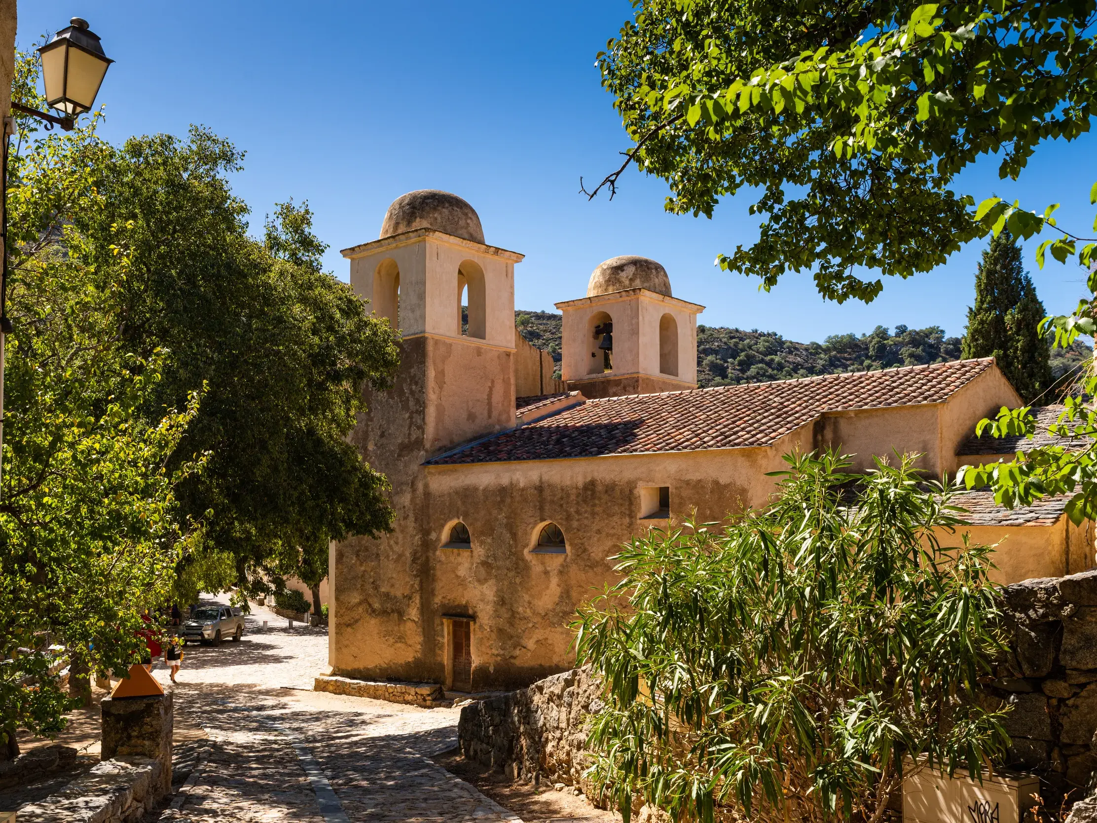 Die romanische Kapelle von Aregno in der Balagne, umgeben von Bäumen an einem sonnigen Wandertag auf Korsika.