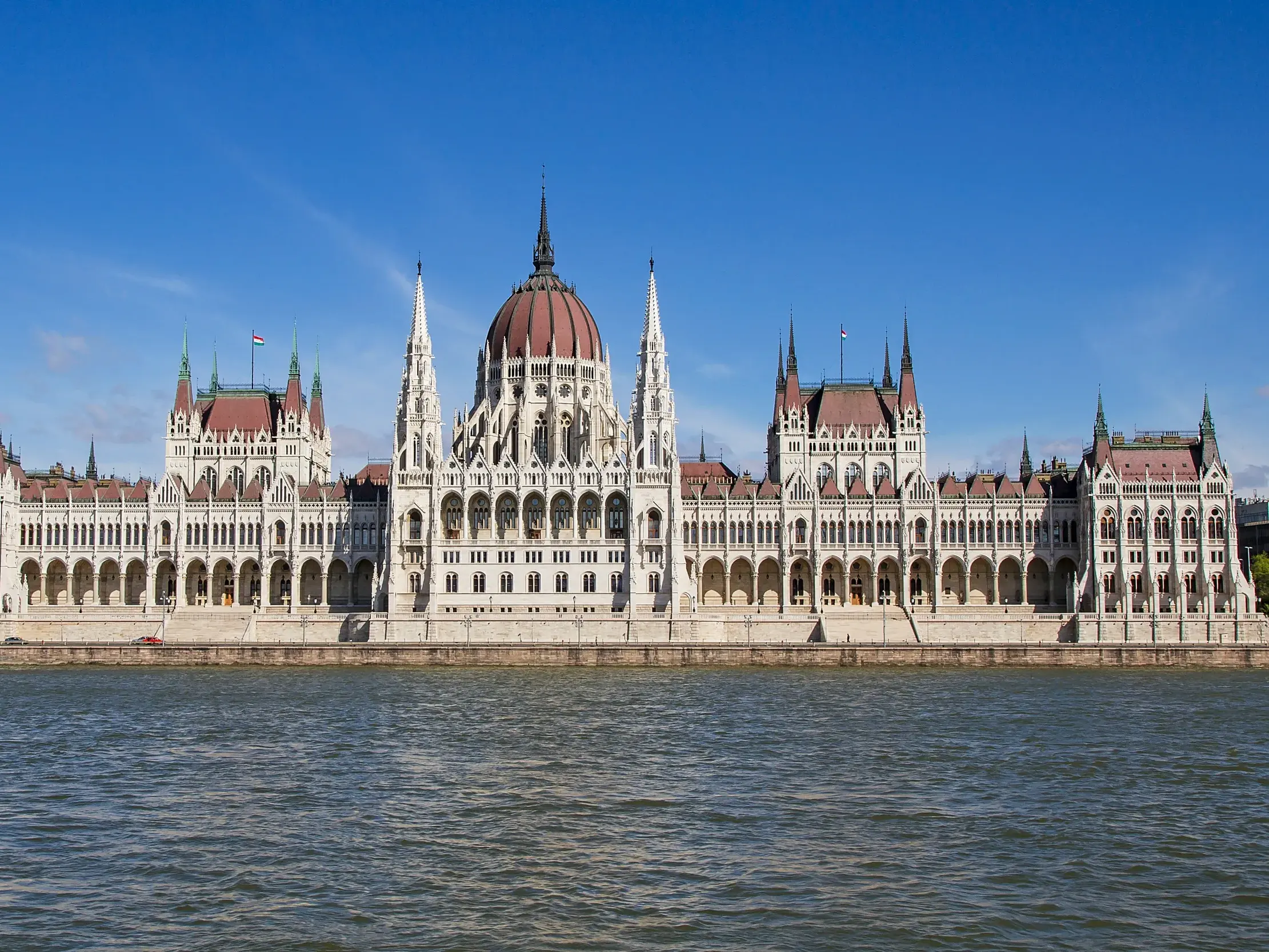 Majestätischer Blick von der Donau auf das monumentale Parlament in Budapest unter einem strahlend blauen Himmel.