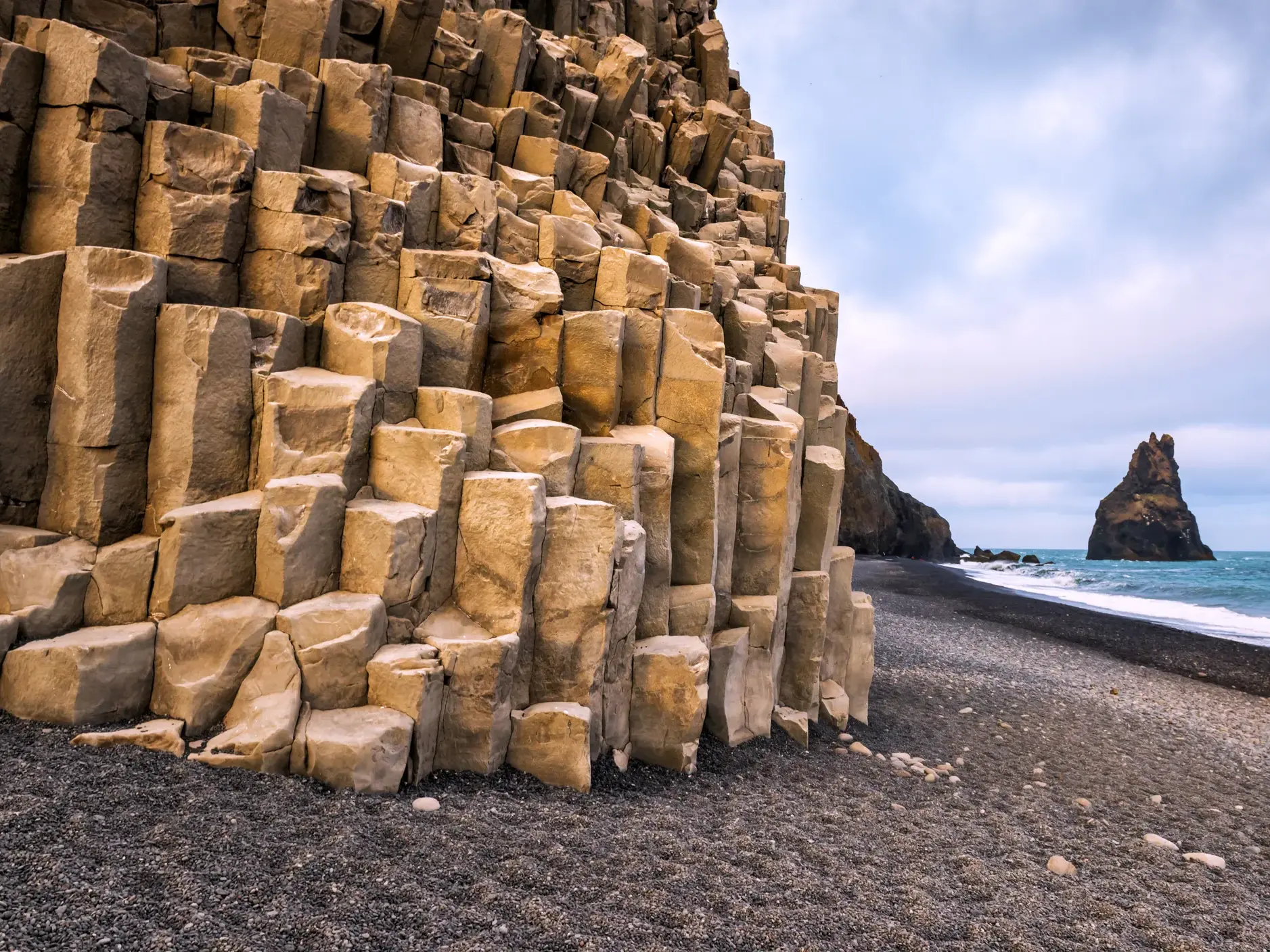 Skurrile Basaltsäulen am schwarzen Lavastrand von Reynisfjara in Südisland mit den Reynisdrangar Felsnadeln im Meer.