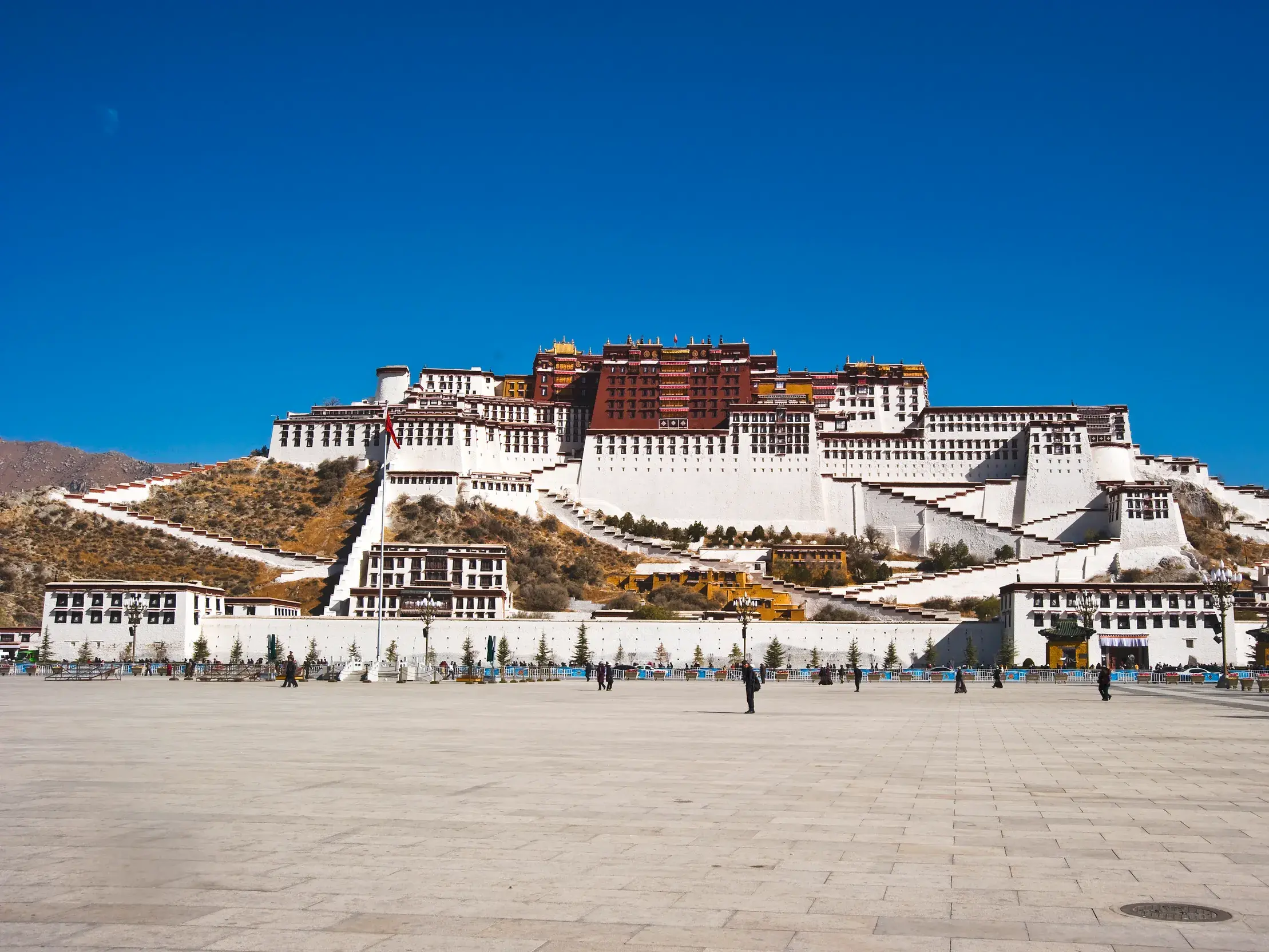 Der monumentale Potala-Palast in Lhasa thront unter strahlend blauem Himmel über einem weiten Platz mit Besuchern.
