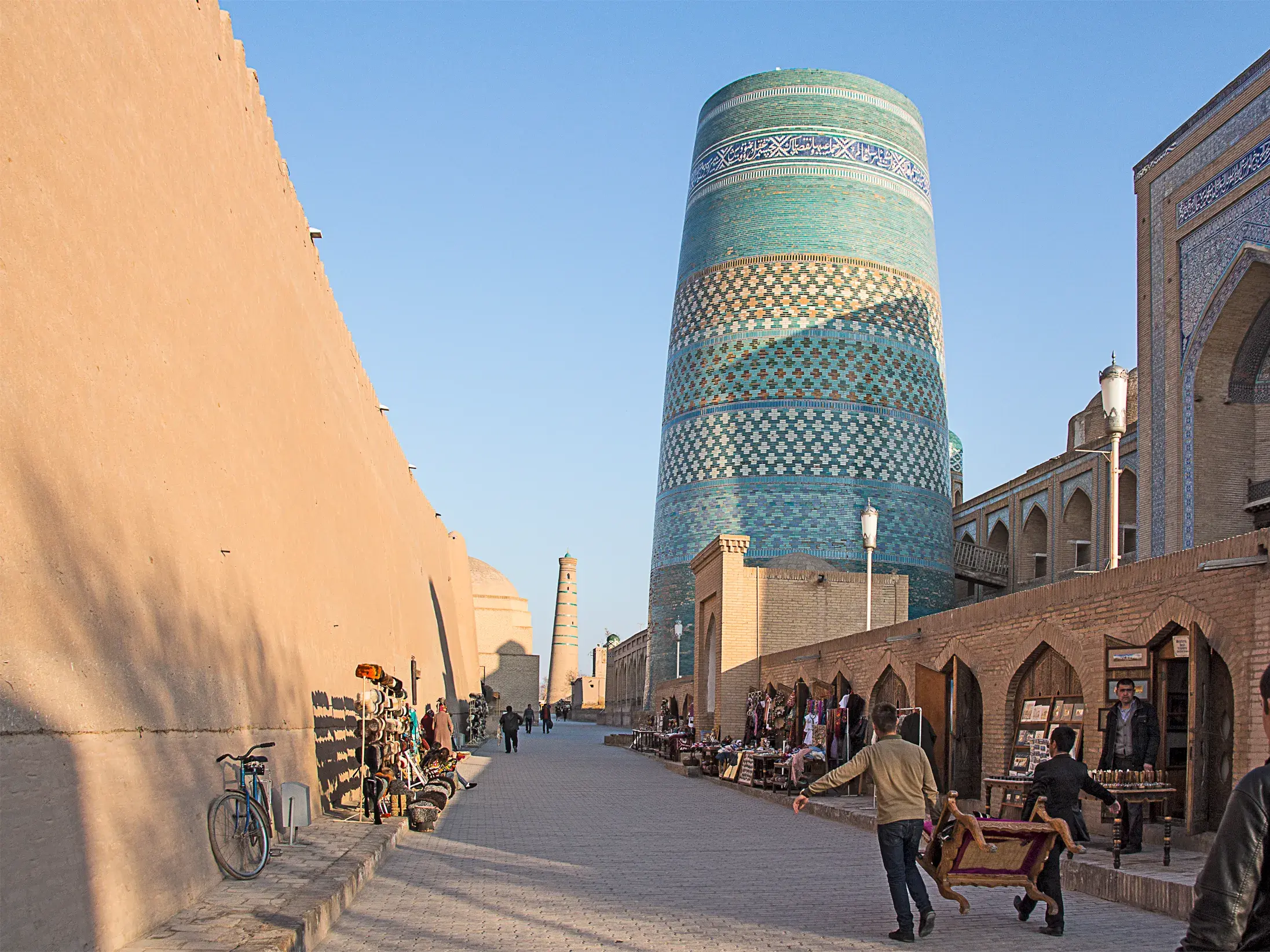 Lebhafte Gasse in Chiwa (UNESCO-Welterbe) mit dem blau gekachelten Kalta Minor Minarett und Händlern am Straßenrand.