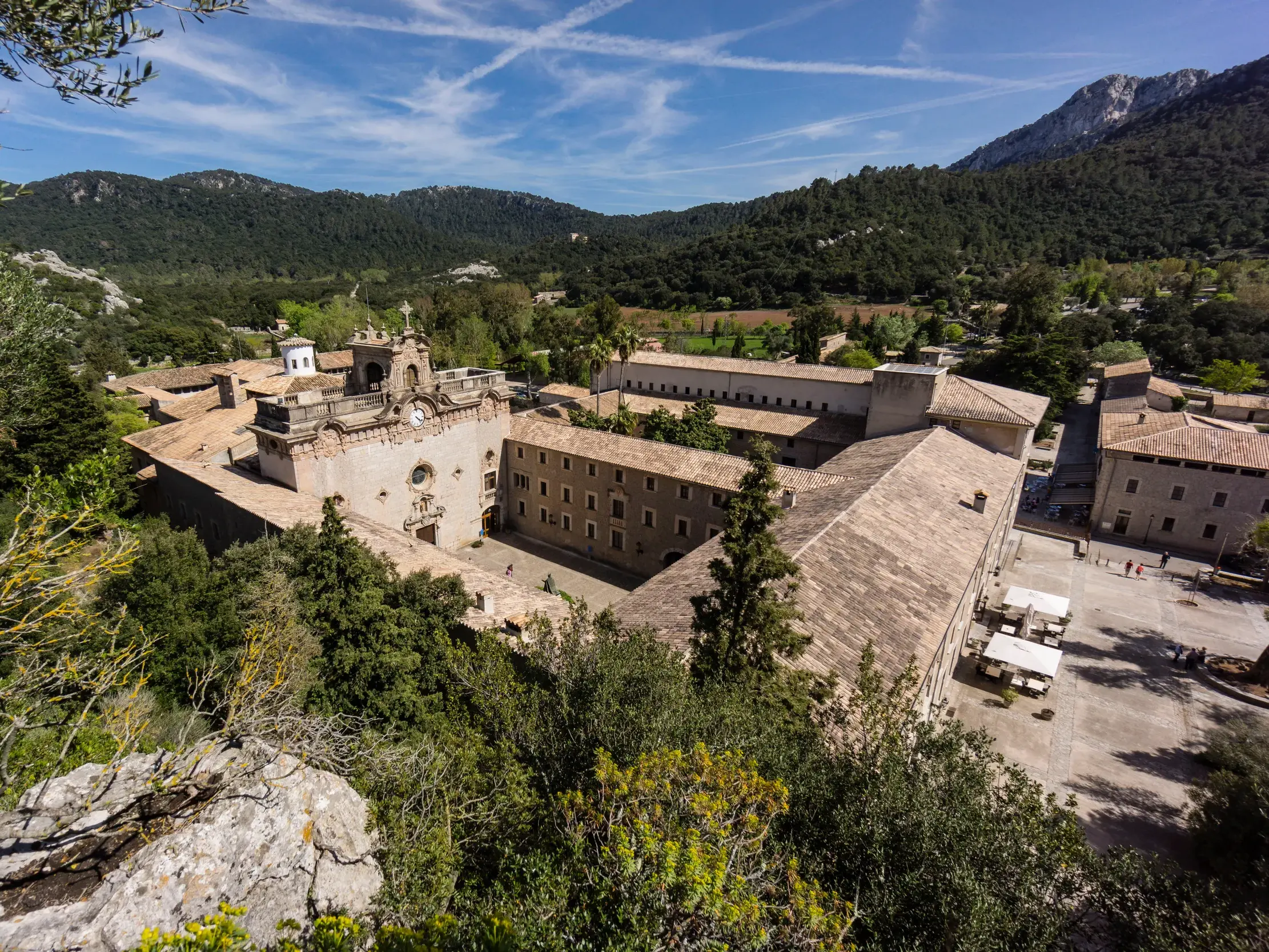 Erhöhte Aussicht von einem Wanderweg auf das historische Kloster Lluc, eingebettet in das grüne Tramuntana-Gebirge.