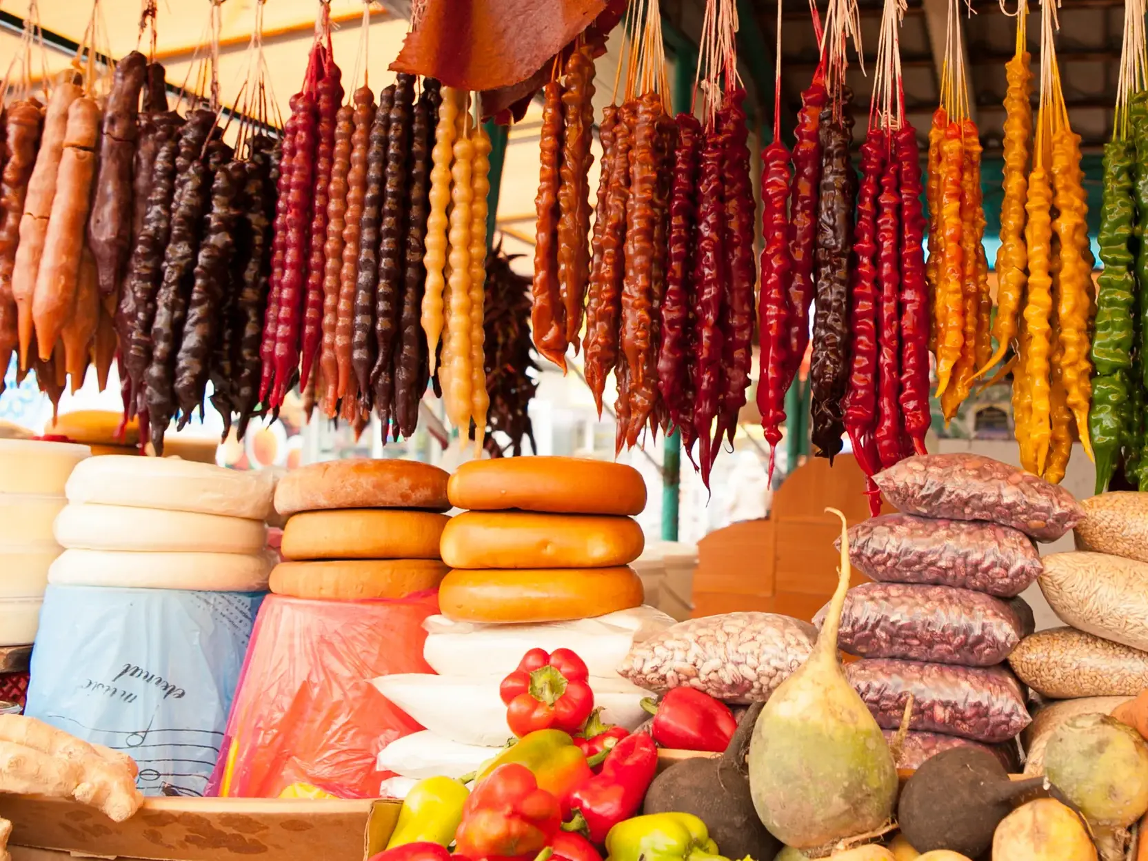 Bunte georgische Spezialität Churchkhela hängt über Käse und frischem Gemüse auf einem lebhaften Marktstand.