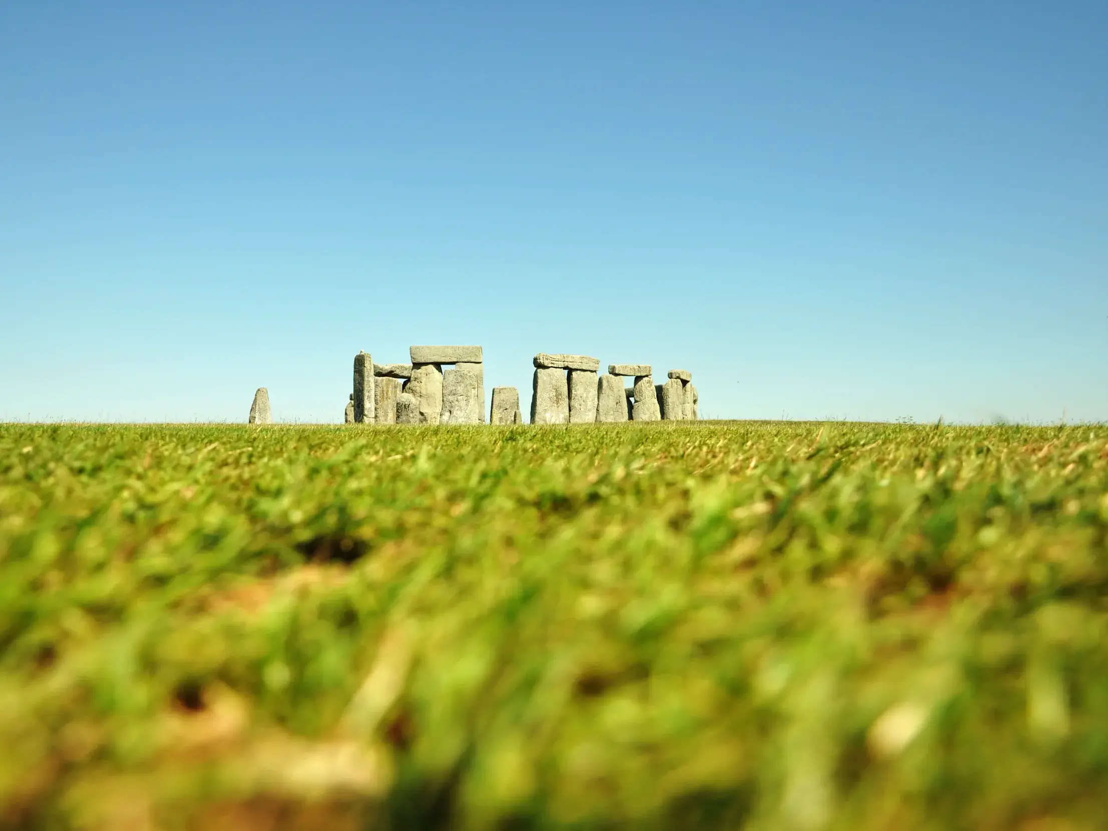Niedriger Blickwinkel über eine saftig grüne Wiese auf die mystischen Steinformationen von Stonehenge an einem sonnigen Tag.