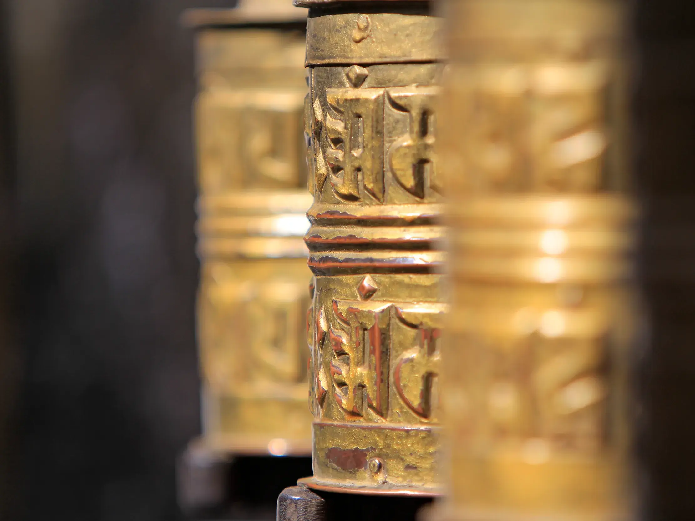 Nahaufnahme von goldenen, reich verzierten Gebetsmühlen in einer Reihe in einem buddhistischen Tempel in Nepal auf einer Rundreise.