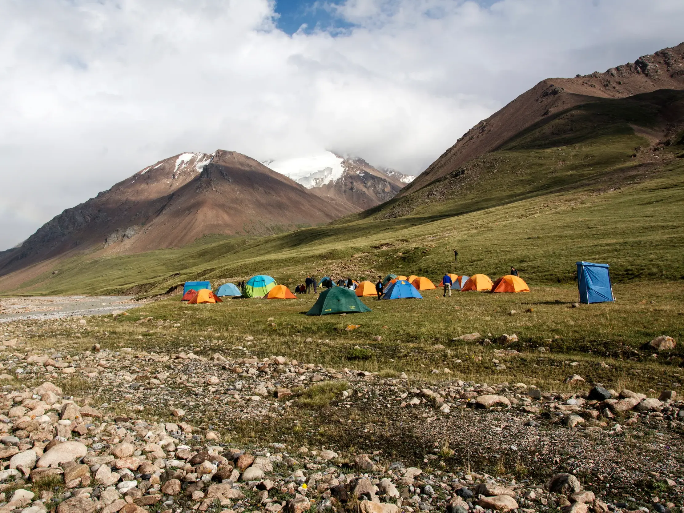 Zelt-Camp einer Reisegruppe auf einer grünen Wiese während eines Trekkings im Terskej-Alatau-Gebirge in Kirgistan.