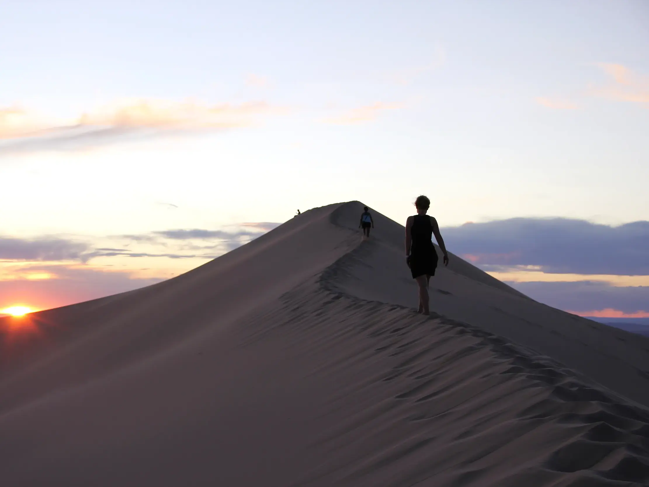 Zwei Wanderer besteigen bei Sonnenuntergang den Kamm der singenden Düne von Khongoryn Els in der Wüste Gobi, Mongolei.