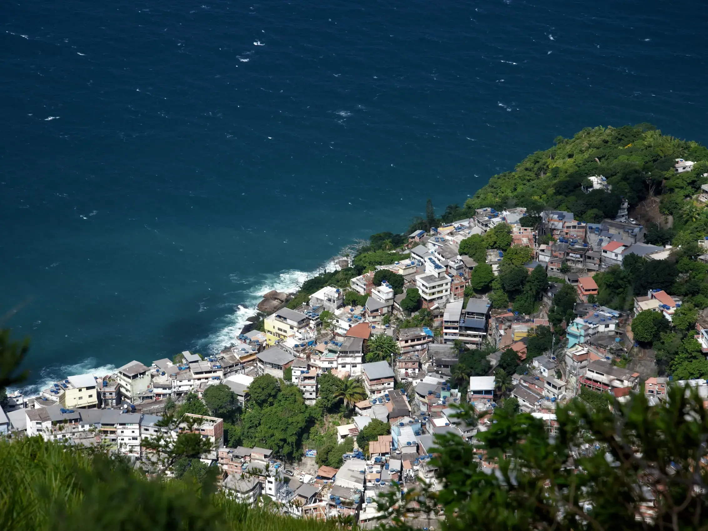 Blick von oben auf die dicht bebaute Favela Morro da Babilônia, die sich an einen grünen Hügel an der Küste von Rio de Janeiro schmiegt.