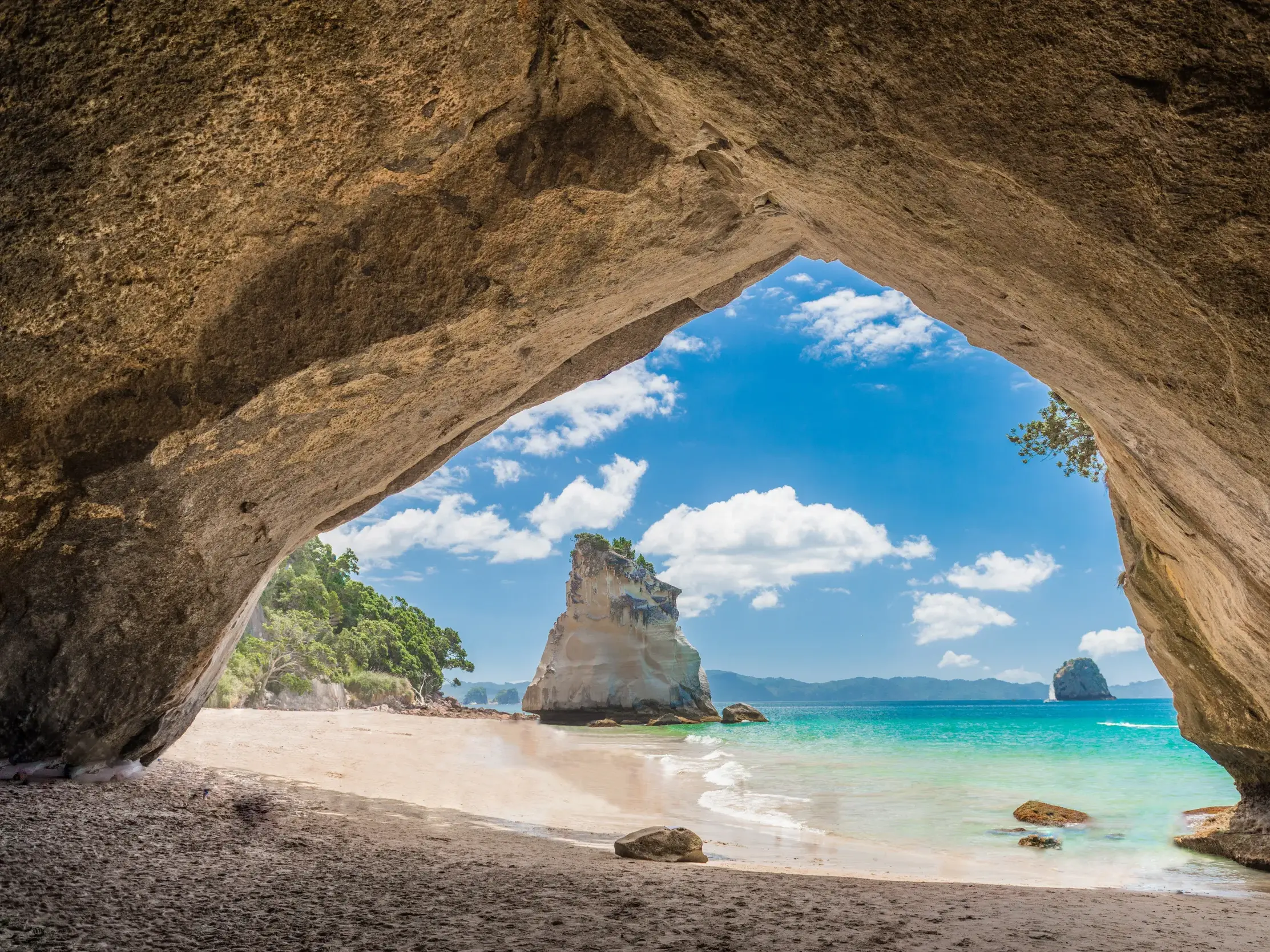 Blick aus einer Felsenhöhle auf die markante Felsformation der Cathedral Cove am Strand der Coromandel-Halbinsel Neuseelands.