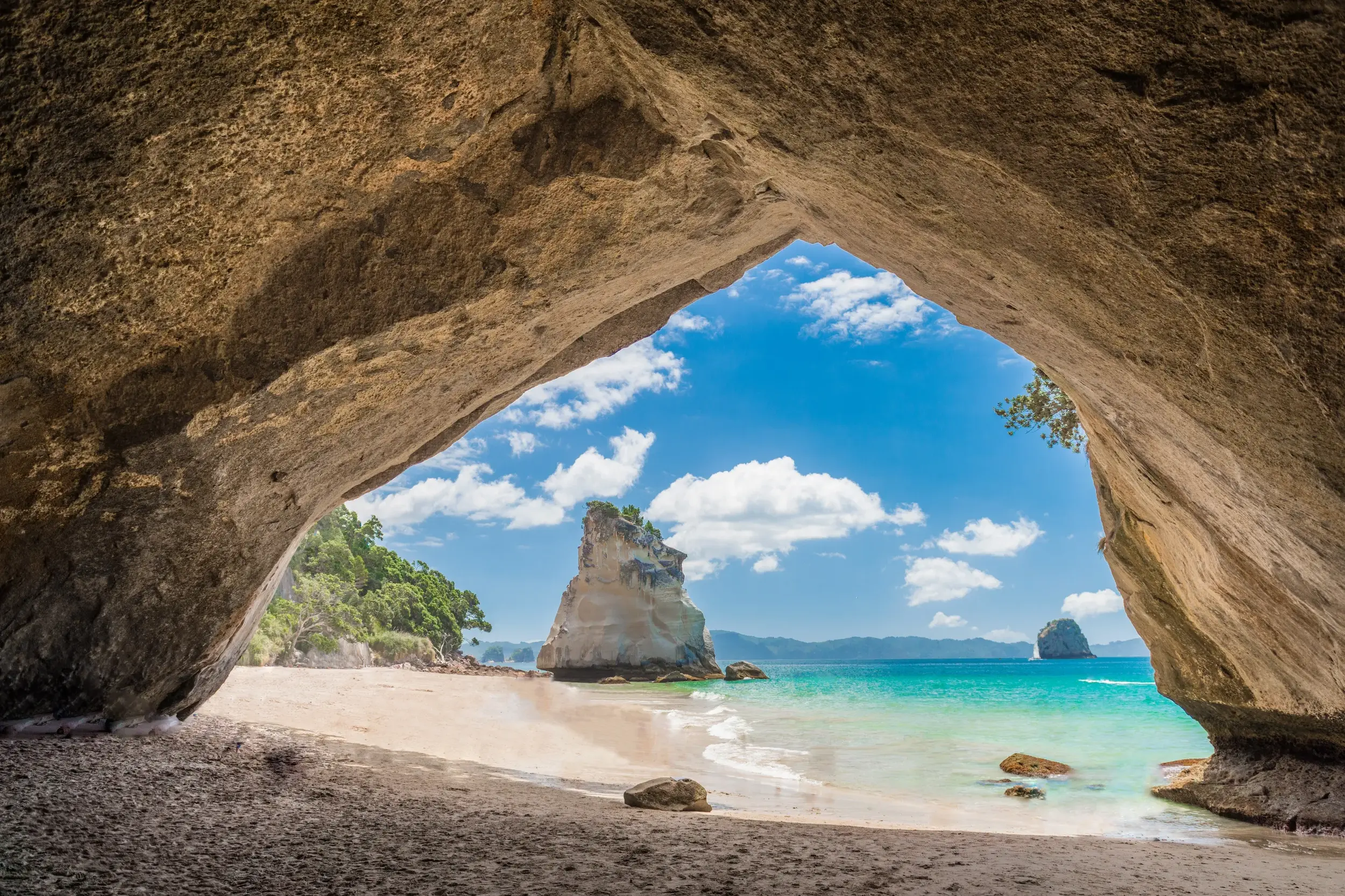 Blick aus einer Felsenhöhle auf die markante Felsformation der Cathedral Cove am Strand der Coromandel-Halbinsel Neuseelands.