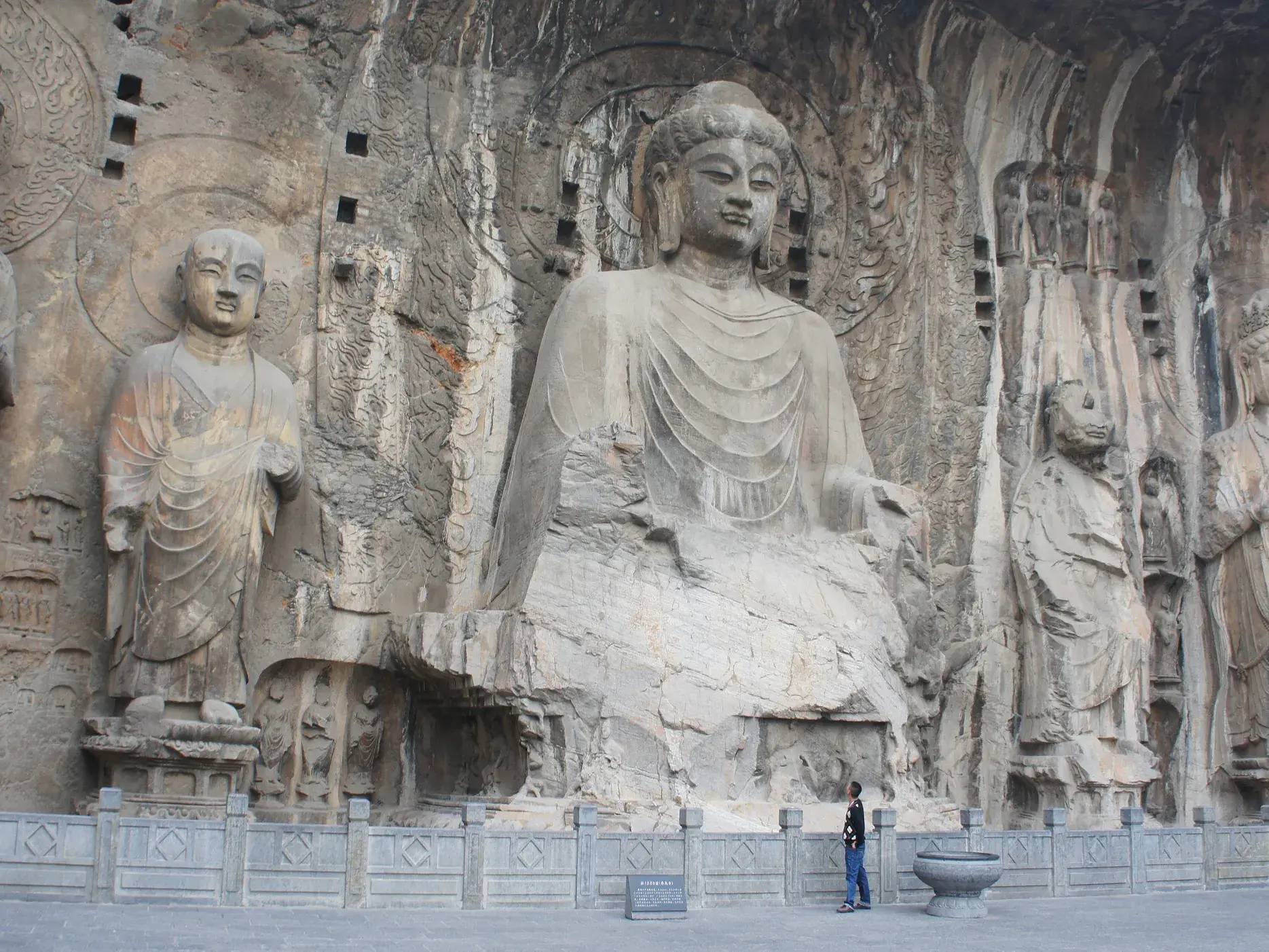 Ein Reisender bestaunt die gewaltigen, in den Fels gehauenen Buddha-Statuen der Longmen-Grotten am Yi-Fluss in China.