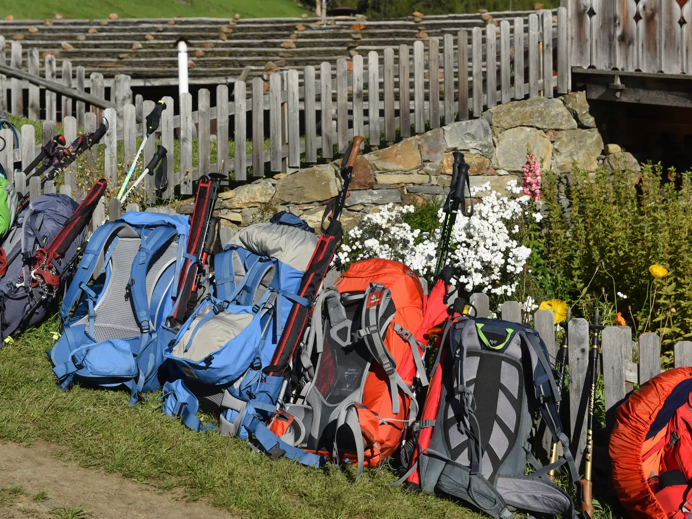 Bunte Wanderrucksäcke mit Stöcken einer Reisegruppe bei einer Rast an einer Almhütte während der Alpenüberquerung.