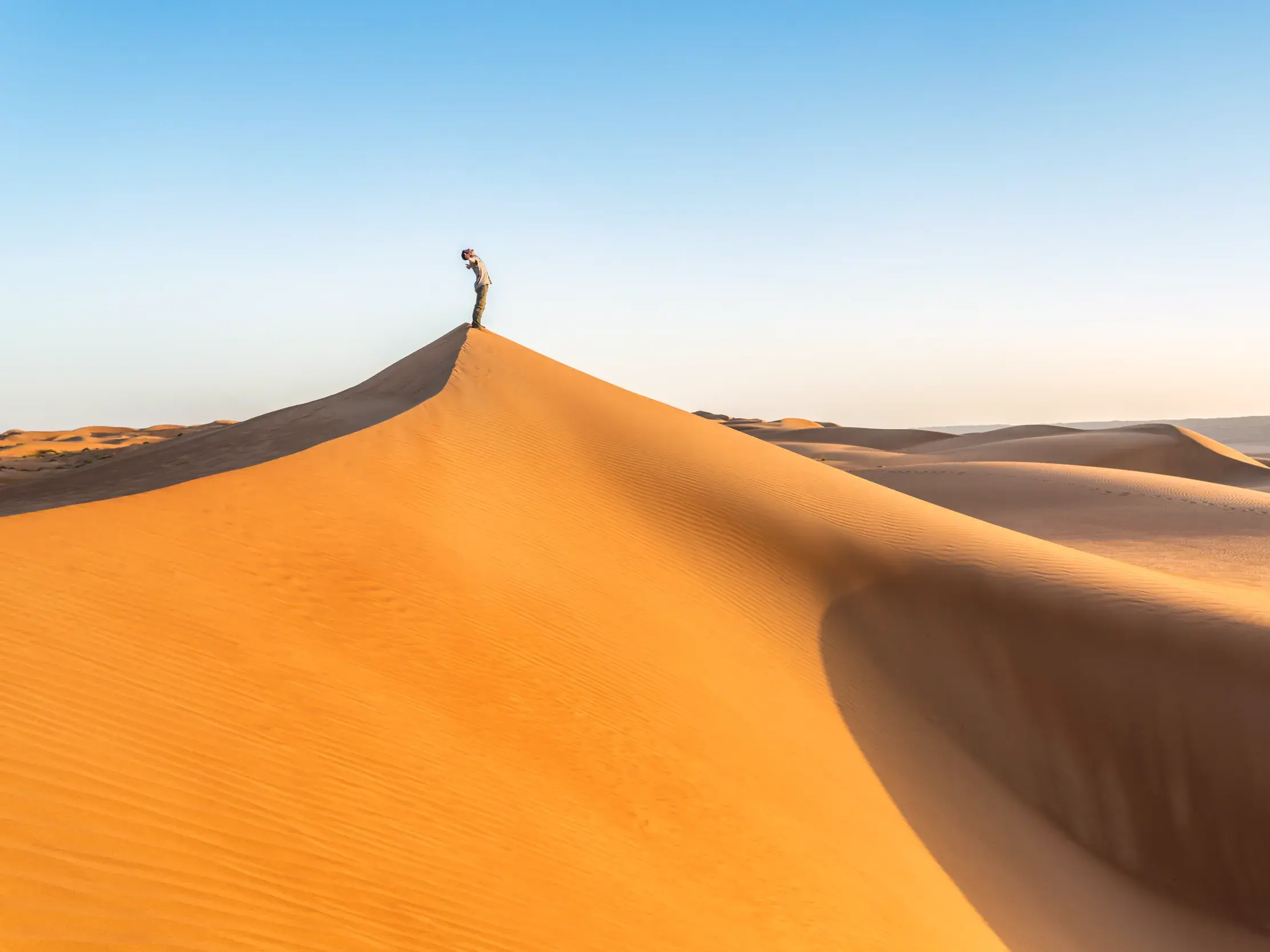 Ein Reisender steht auf dem Kamm einer hohen Düne und blickt über die endlose Sandlandschaft der Wahiba-Wüste im Oman.
