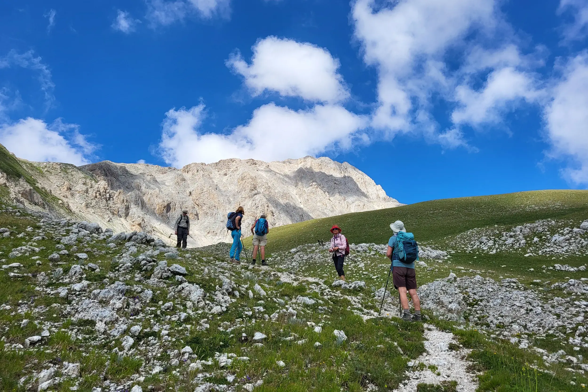 Eine Hauser Wandergruppe auf einem steinigen Pfad beim Aufstieg im Nationalpark Gran Sasso unter blauem Himmel mit Wolken.