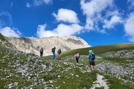 Eine Hauser Wandergruppe auf einem steinigen Pfad beim Aufstieg im Nationalpark Gran Sasso unter blauem Himmel mit Wolken.