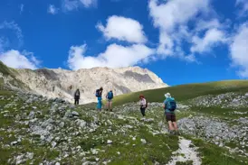 Eine Hauser Wandergruppe auf einem steinigen Pfad beim Aufstieg im Nationalpark Gran Sasso unter blauem Himmel mit Wolken.