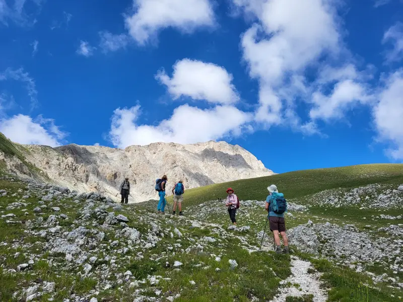 Eine Hauser Wandergruppe auf einem steinigen Pfad beim Aufstieg im Nationalpark Gran Sasso unter blauem Himmel mit Wolken.