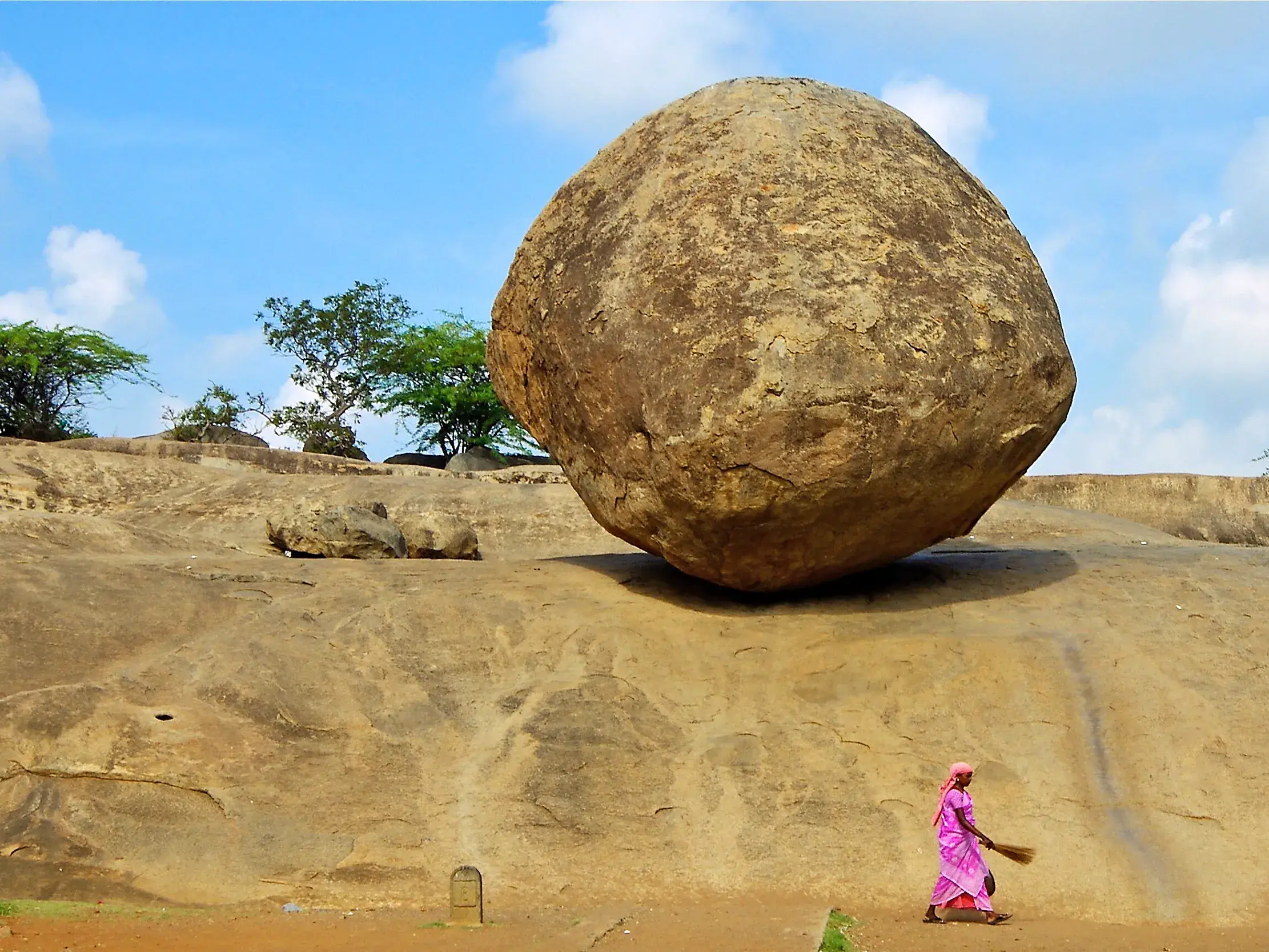 Frau in pinkem Sari fegt vor dem balancierenden Felsen Krishnas Butterball in Mahabalipuram auf einer Studienreise in Indien.