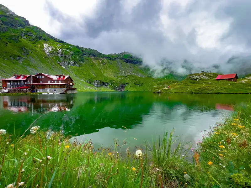 Die malerische Balea-See-Hütte am smaragdgrünen Bergsee, umgeben von den nebligen Gipfeln des Fagaras-Gebirges in Rumänien.