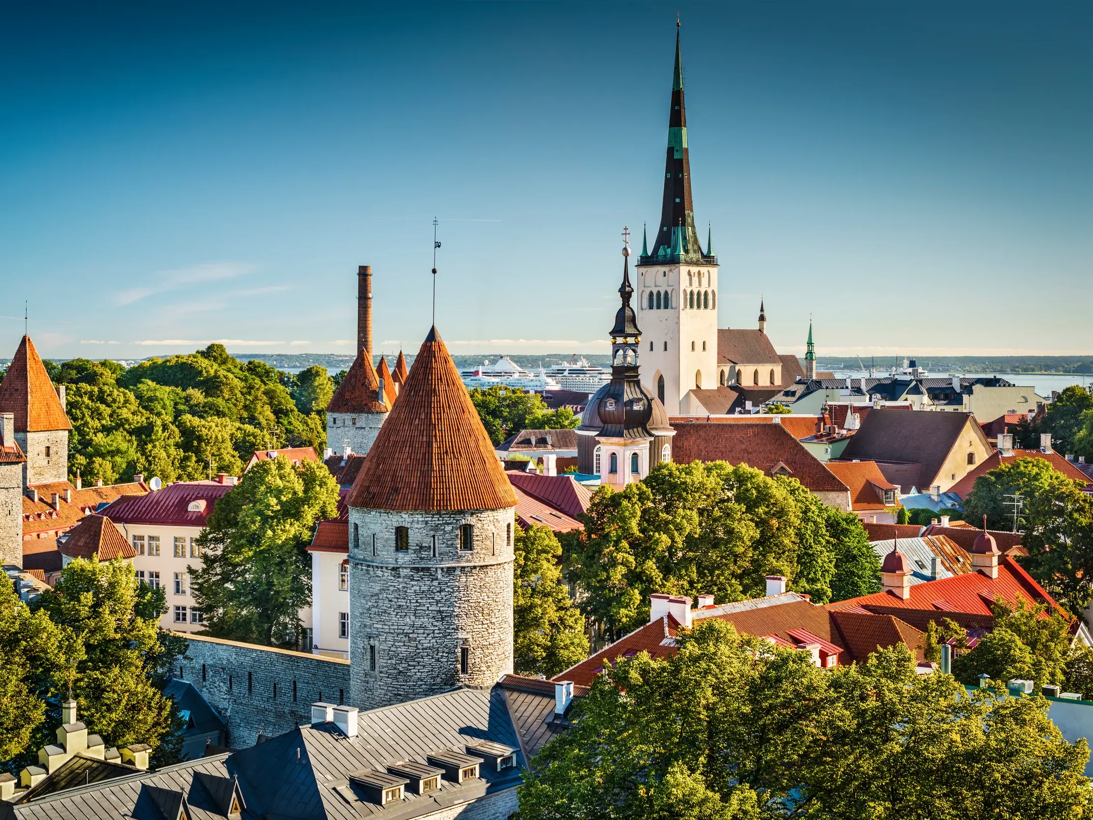 Historische Stadtmauer und Türme der Altstadt von Tallinn unter blauem Himmel, mit der Ostsee im Hintergrund.