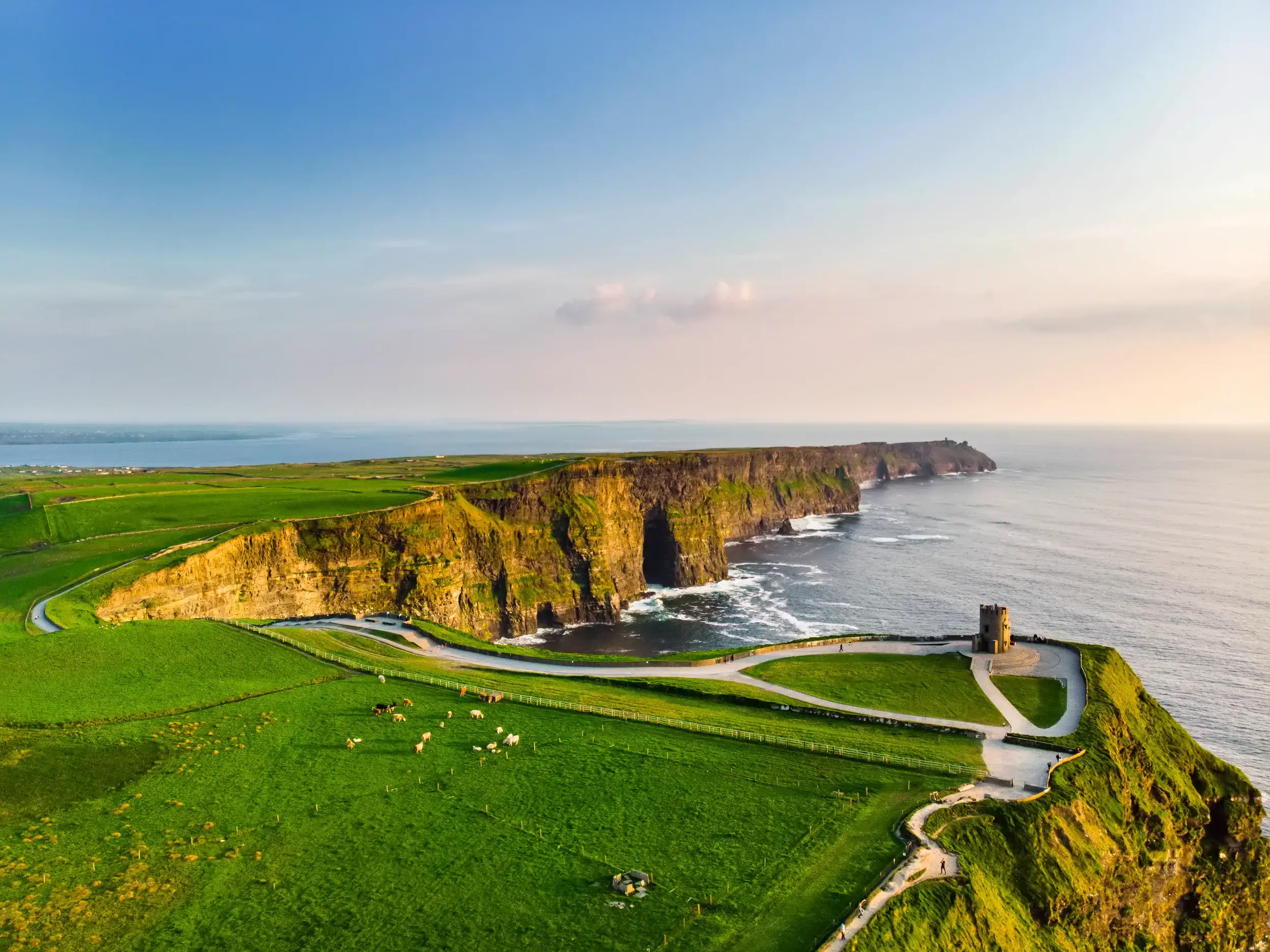 Eindrucksvolle Steilküste der Klippen von Moher in Irland mit grünen Weiden und einem alten Steinturm am tosenden Atlantik.