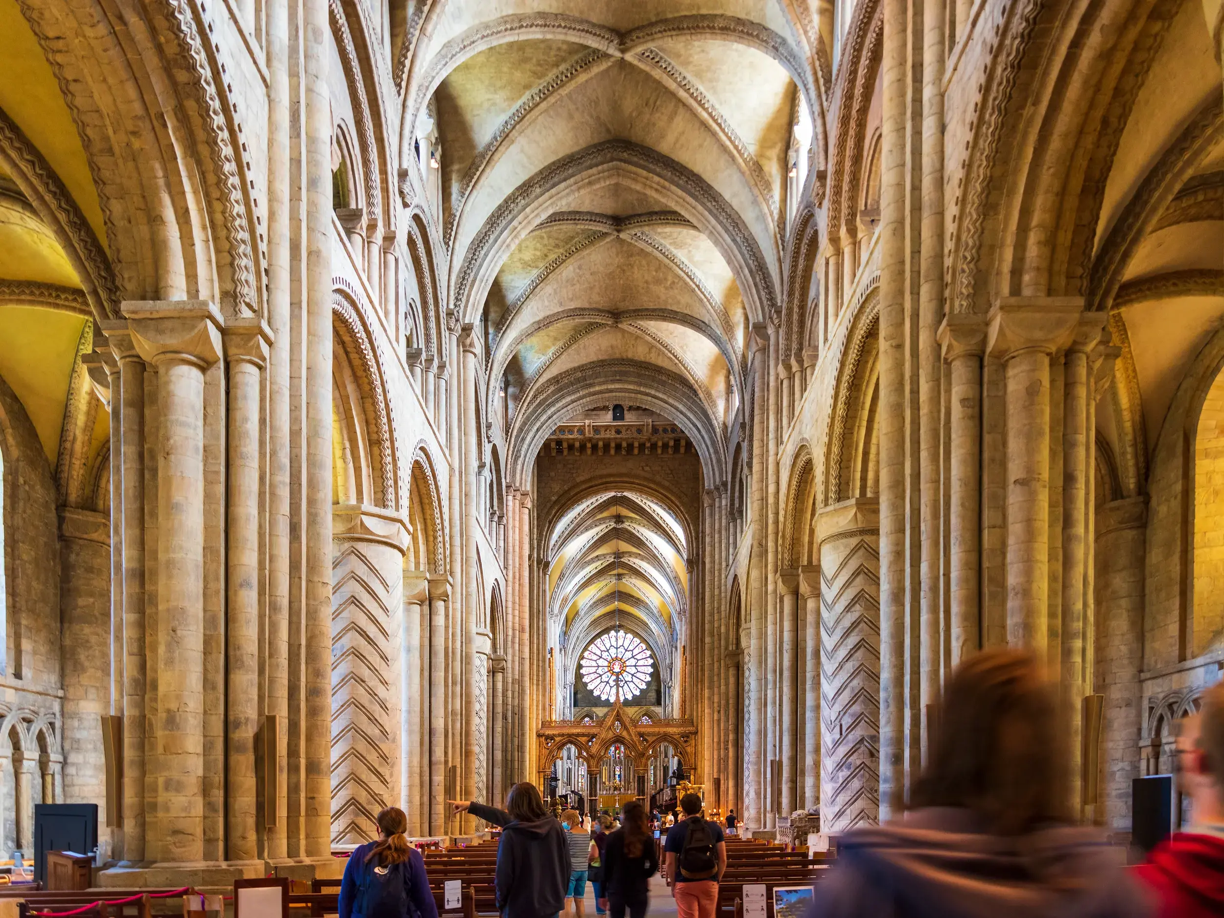 Reisegruppe im imposanten Langhaus der normannischen Durham Cathedral, eine Frau zeigt auf die hohen, verzierten Gewölbedecken.