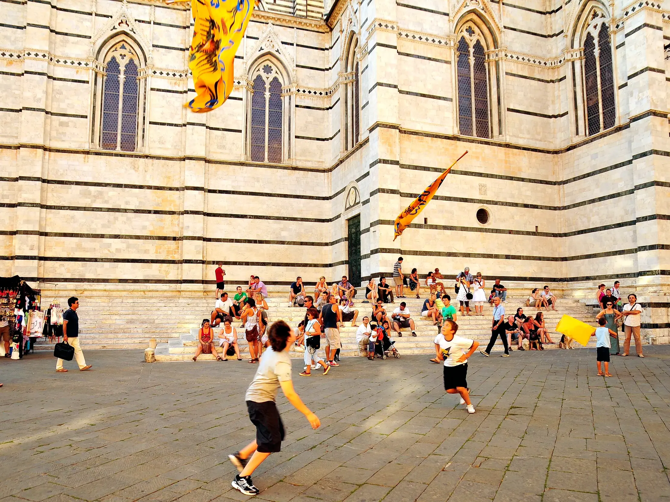 An einem sonnigen Tag in Siena spielen Kinder vor der gestreiften Marmorfassade des Doms, dem Ziel der Toskana-Wanderung.