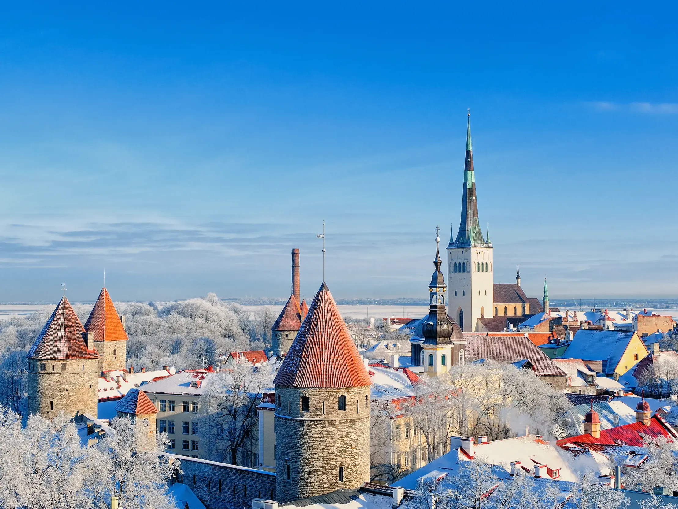 Ausblick vom Domberg auf die verschneite Altstadt von Tallinn mit den Türmen der Stadtmauer und der Olaikirche im Winter.