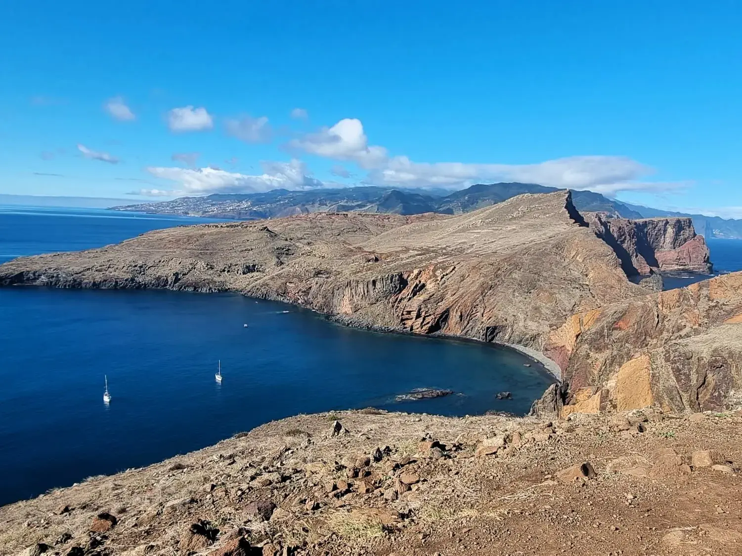 Sonnige Aussicht von einem Wanderweg auf die karge Felsküste des Cabo São Lourenço auf Madeira mit Segelbooten im blauen Atlantik.