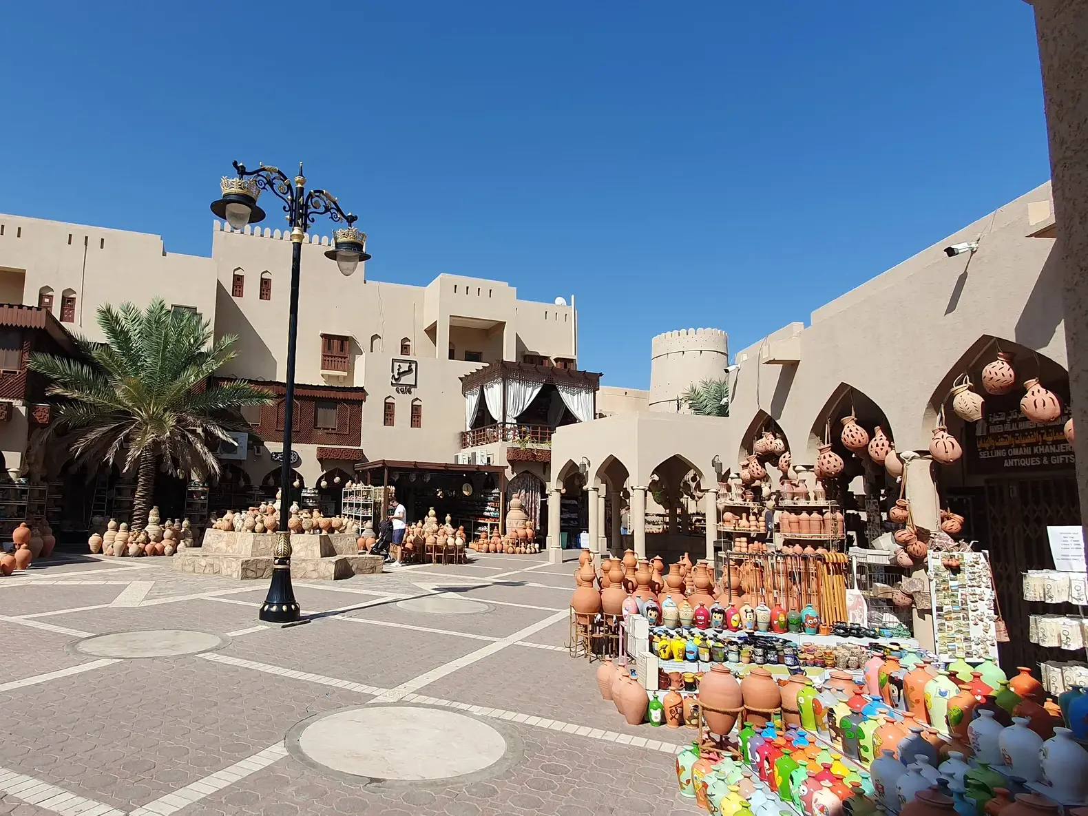 Sonniger Innenhof im Souk von Nizwa im Oman, gefüllt mit Ständen, die bunte, handgefertigte Keramik und Töpferwaren verkaufen.