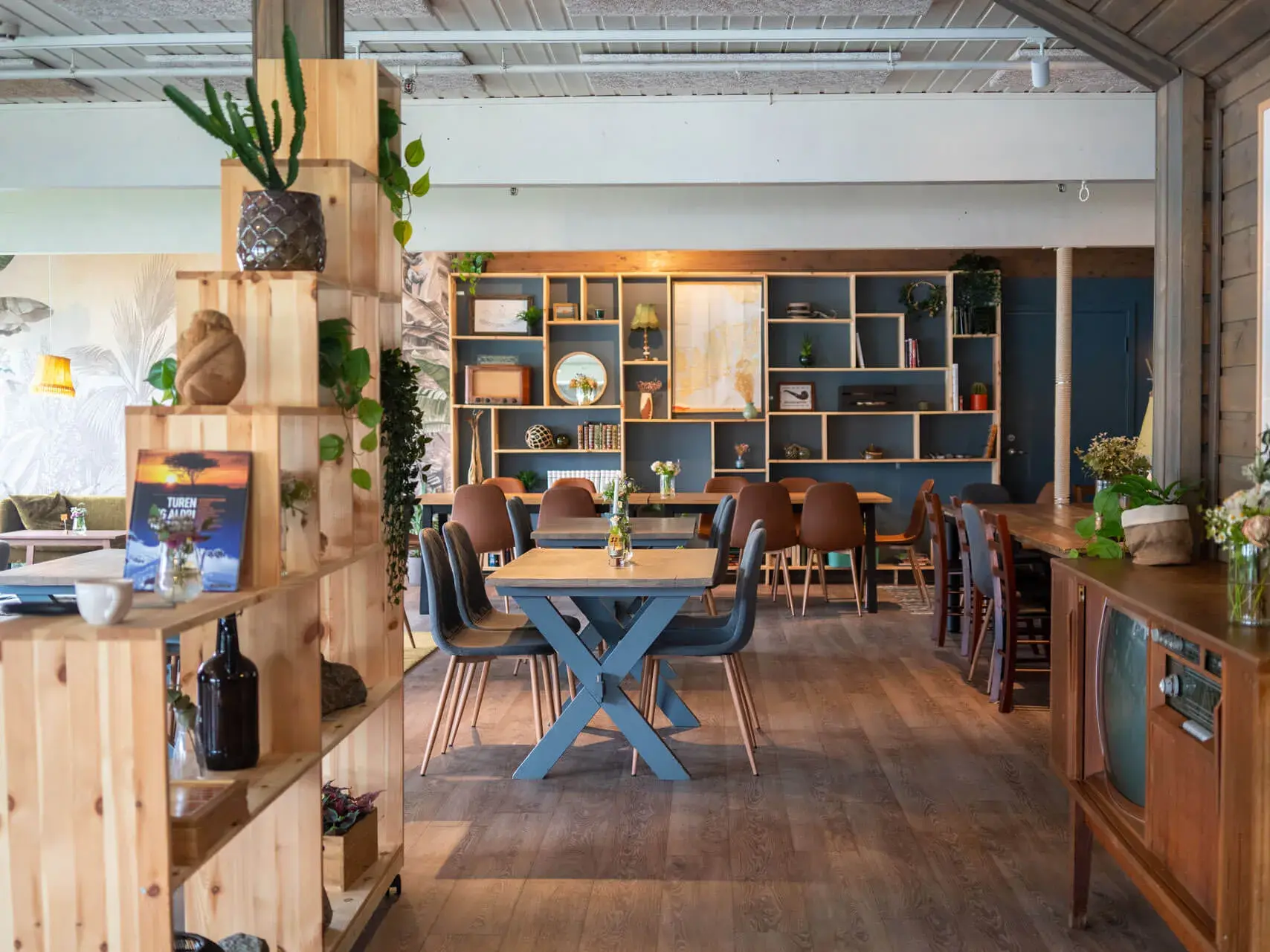 Gemütlicher Gastraum im Café des Biohofs Lofoten Gårdsysteri mit Tischen und Regalen aus hellem Holz.