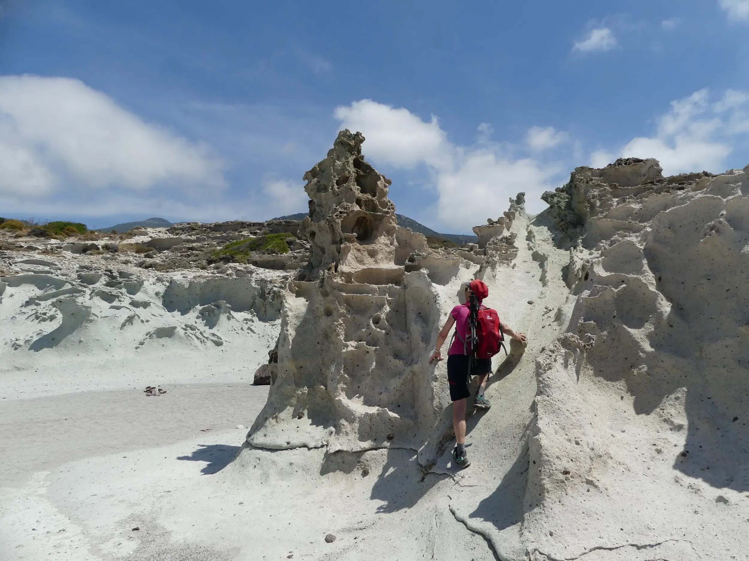 Wanderin mit Rucksack erkundet auf einem schmalen Pfad die bizarr geformten, weißen Granitfelsen am Capo Testa auf Sardinien.