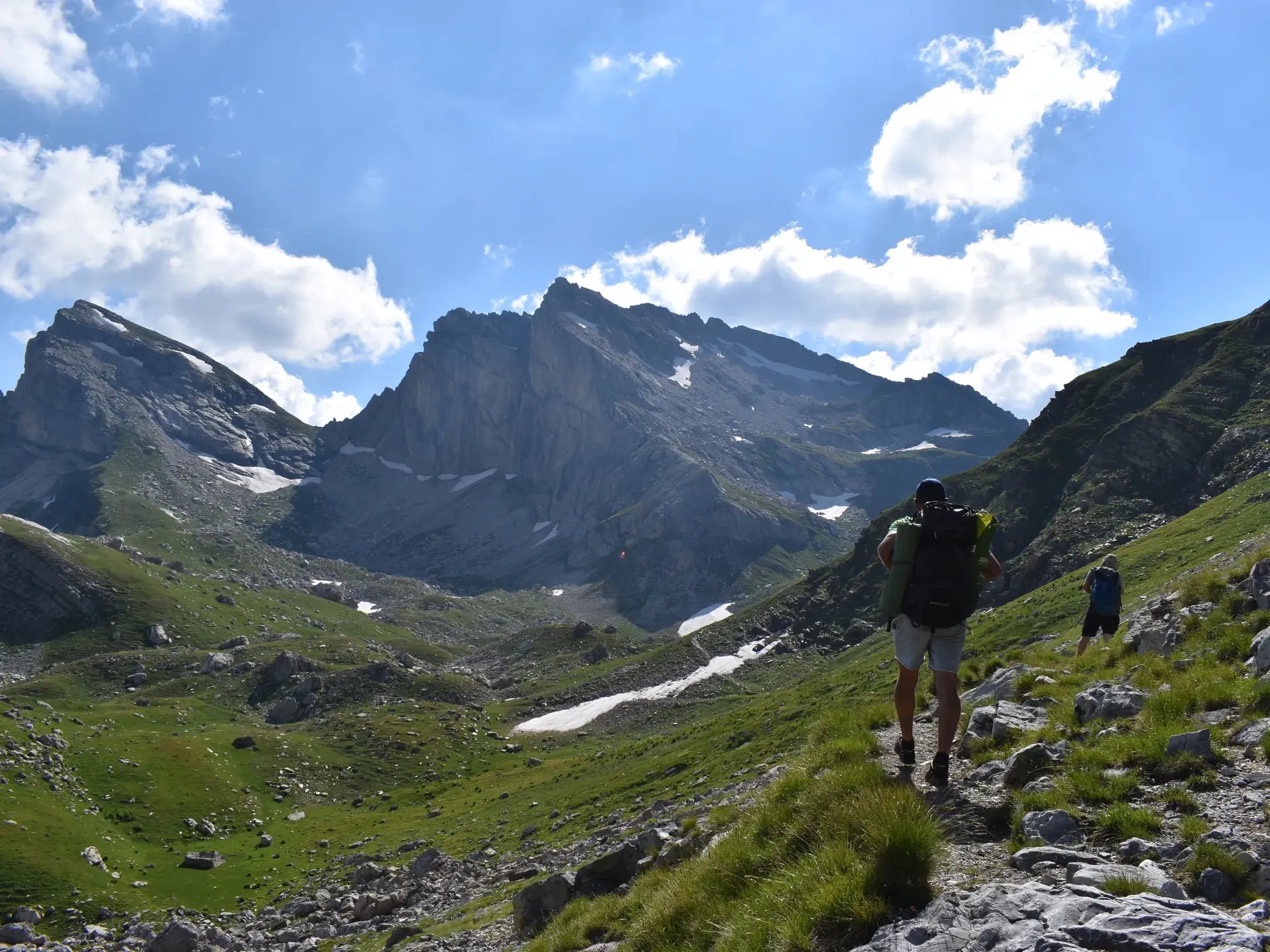 Zwei Wanderer mit großen Rucksäcken beim Trekking auf einem Bergpfad im Korab-Gebirge vor einem Panorama schroffer Gipfel.
