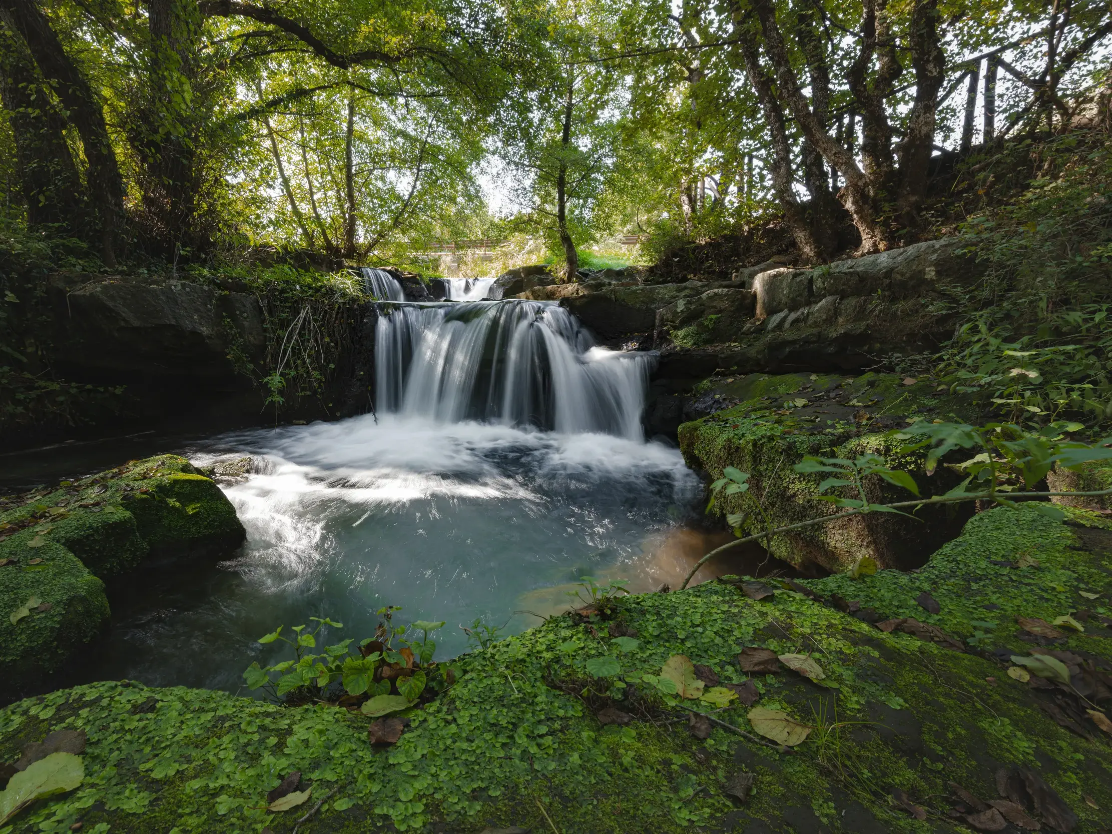 Der Monti Gelato Wasserfall auf der Via Francigena, wo das Wasser über moosbedeckte Felsen in ein klares, türkises Becken fließt.