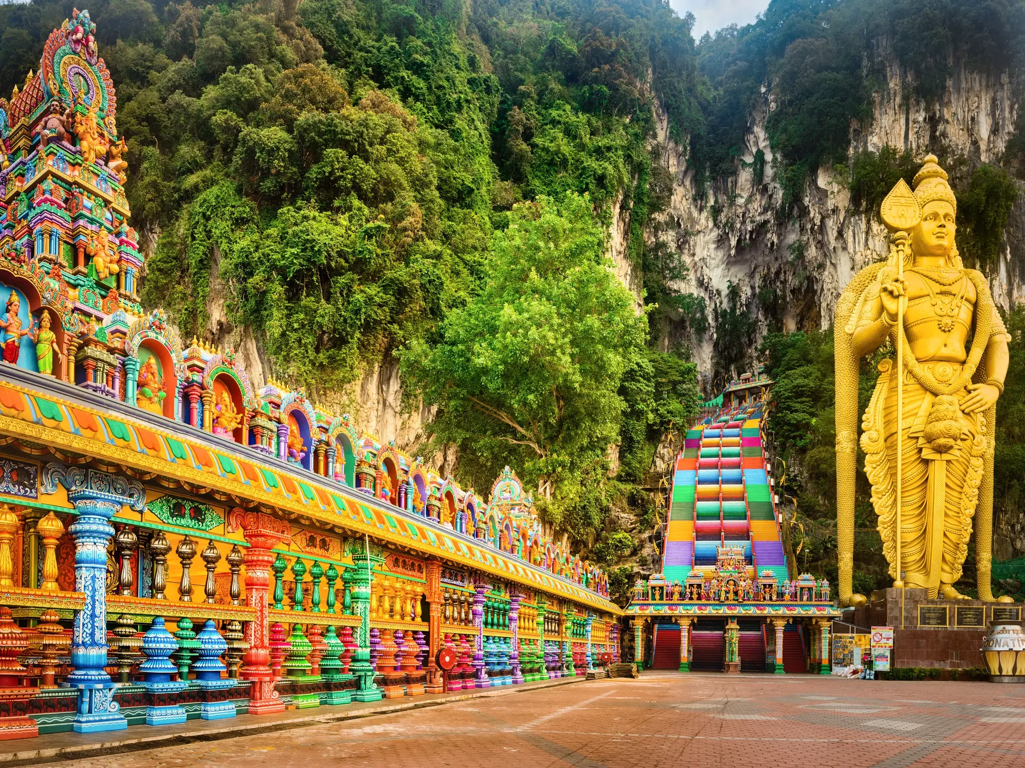 Goldene Statue von Lord Murugan vor der bunten Treppe und dem farbenfrohen Hindu-Heiligtum der Batu-Höhlen in Malaysia.