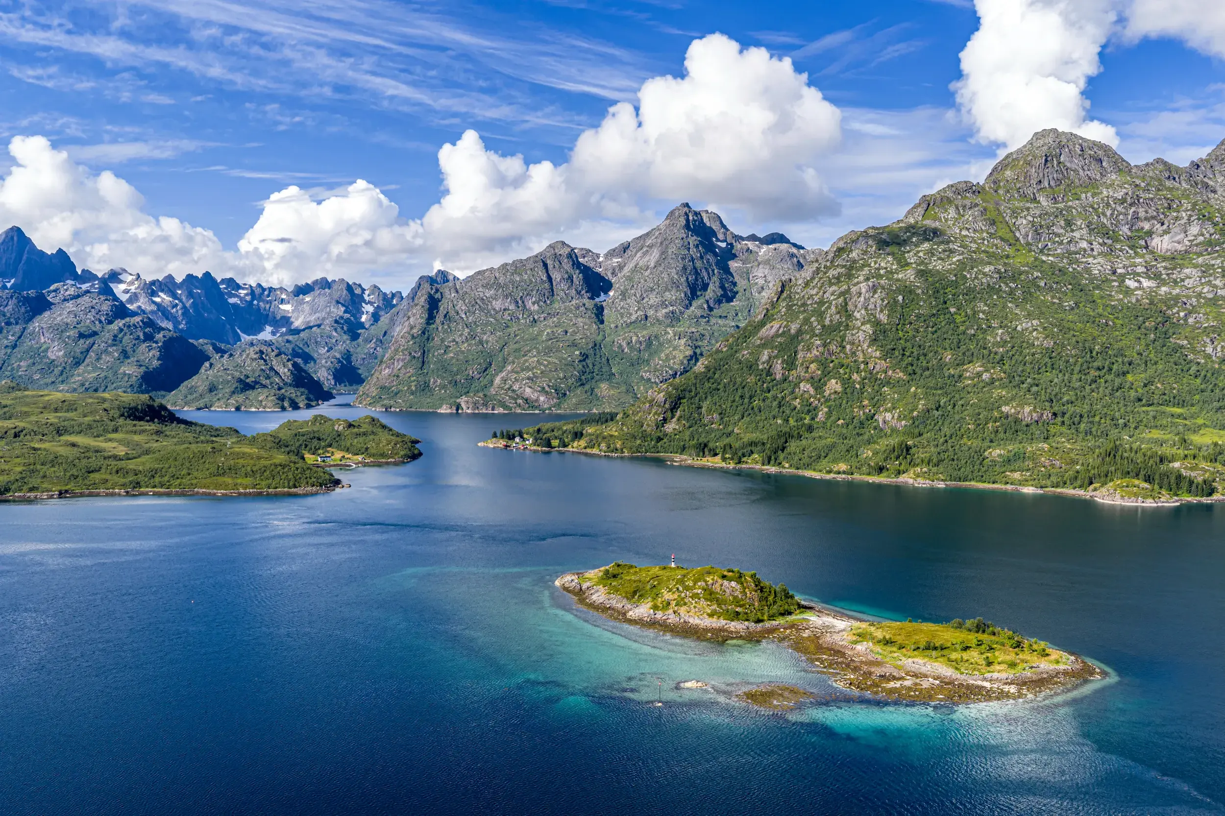 Panoramablick auf die Fjordlandschaft der Lofoten mit kleinen Inseln im tiefblauen Wasser und einer schneebedeckten Bergkette.