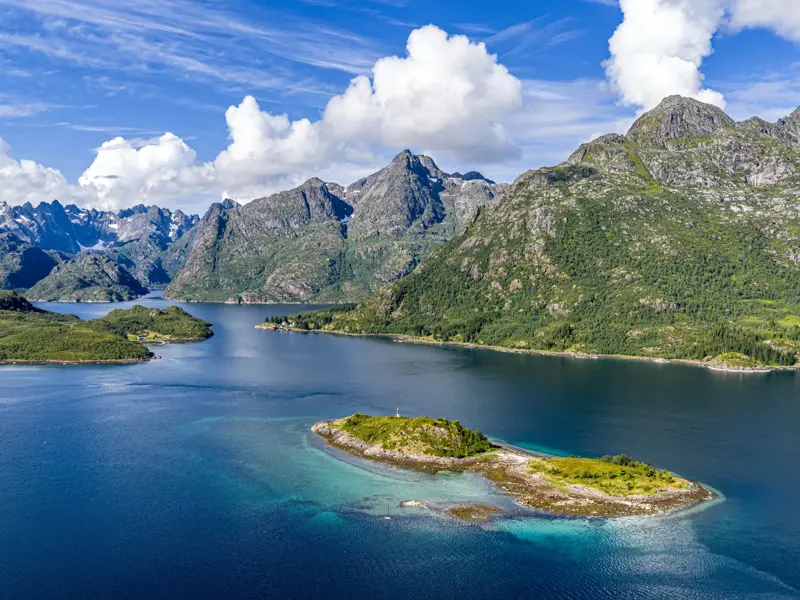 Panoramablick auf die Fjordlandschaft der Lofoten mit kleinen Inseln im tiefblauen Wasser und einer schneebedeckten Bergkette.