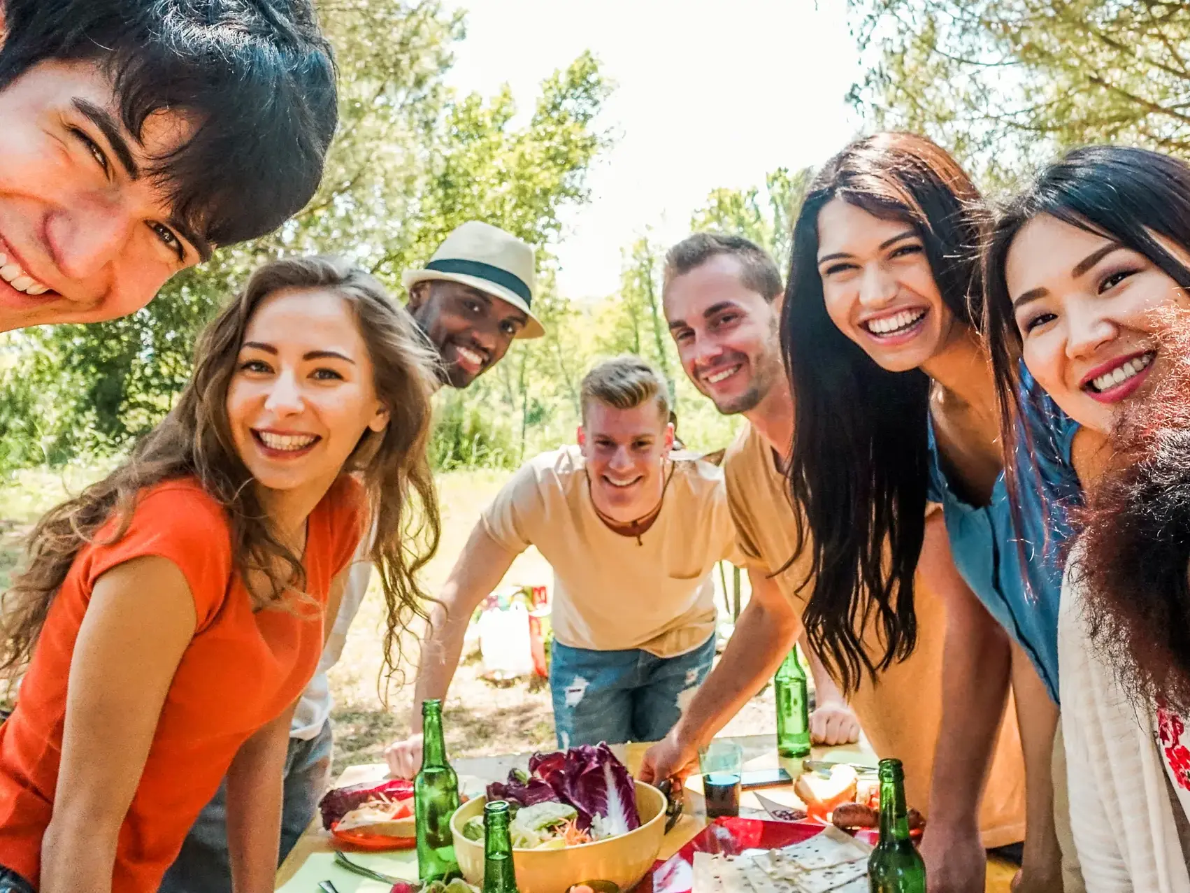 Eine diverse Gruppe junger Leute macht bei einer Gruppenreise ein fröhliches Selfie während eines Picknicks in der Natur.