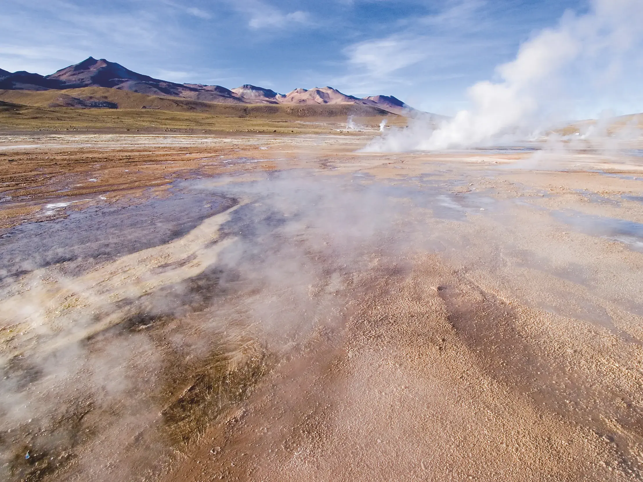 Dampfende Fontänen auf dem Tatio-Geysirfeld in der Atacama-Wüste Chiles vor der weiten Kulisse der Anden.