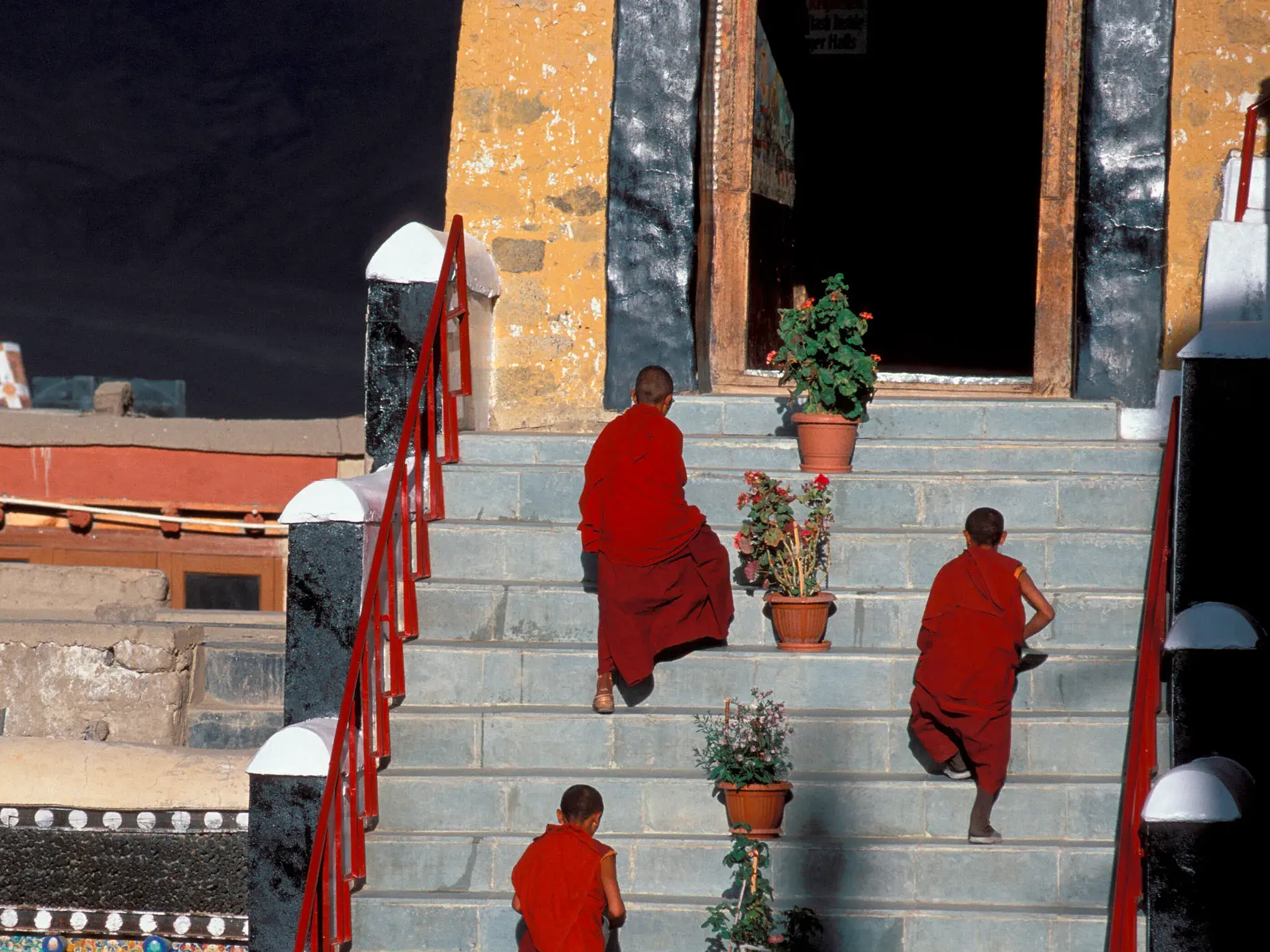 Buddhistische Mönche in traditionellen roten Gewändern auf dem Weg in einen Tempel eines Klosters in der Bergwelt Ladakhs.