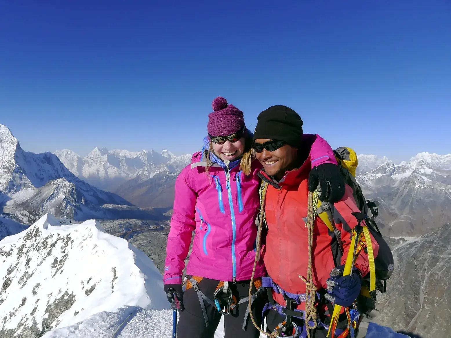 Eine Bergsteigerin und ihr Guide umarmen sich glücklich auf dem Gipfel des Island Peak mit Blick auf den Ama Dablam in Nepal.