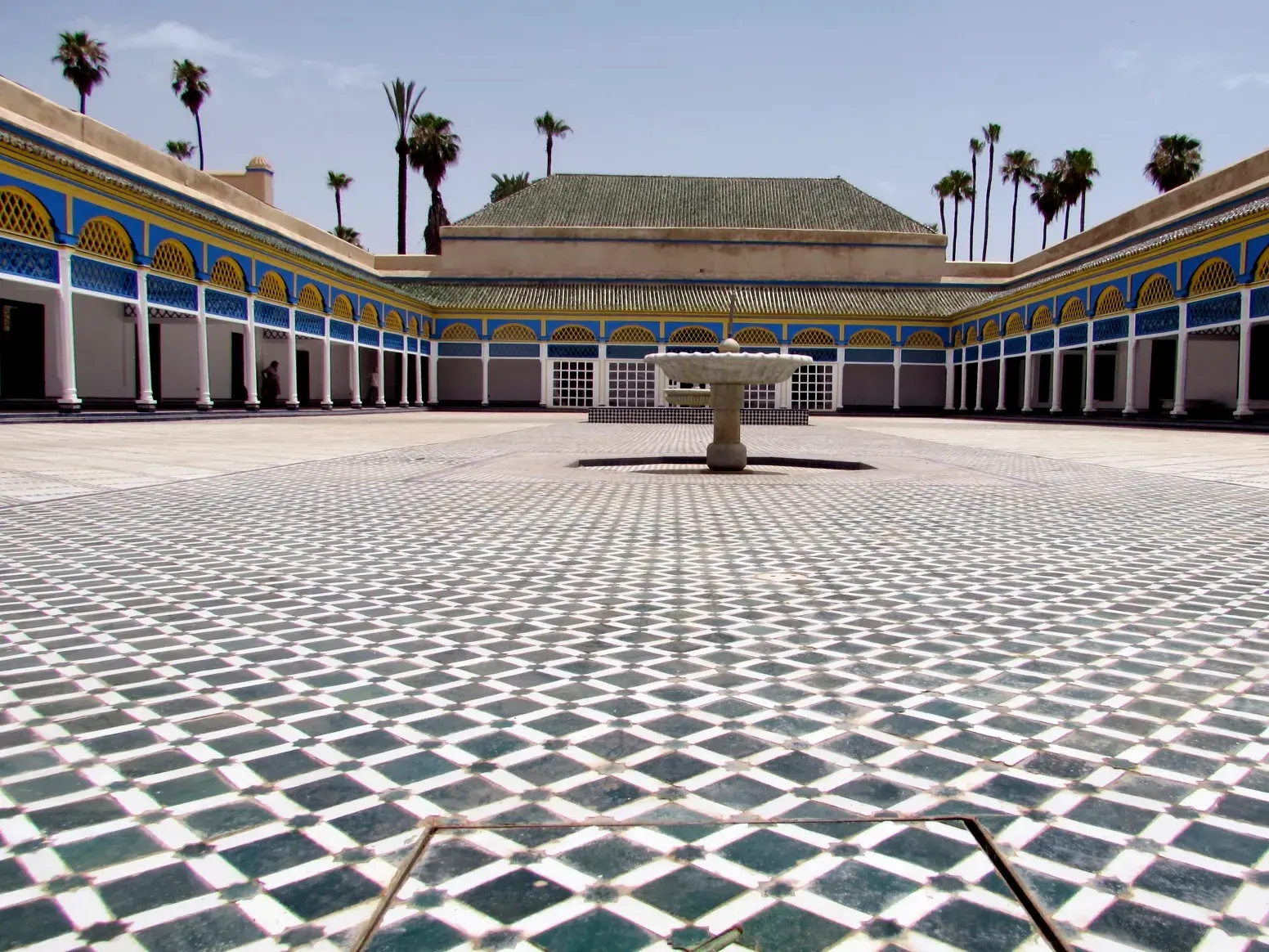Weitläufiger Innenhof des Bahia-Palasts in Marrakesch mit kunstvollen Mosaikböden, verzierten Arkaden und einem Brunnen.
