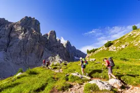 Wandergruppe mit Rucksäcken auf einem schmalen Pfad des Höhenwegs Alta Via 1 entlang schroffer Felsen der Dolomiten.