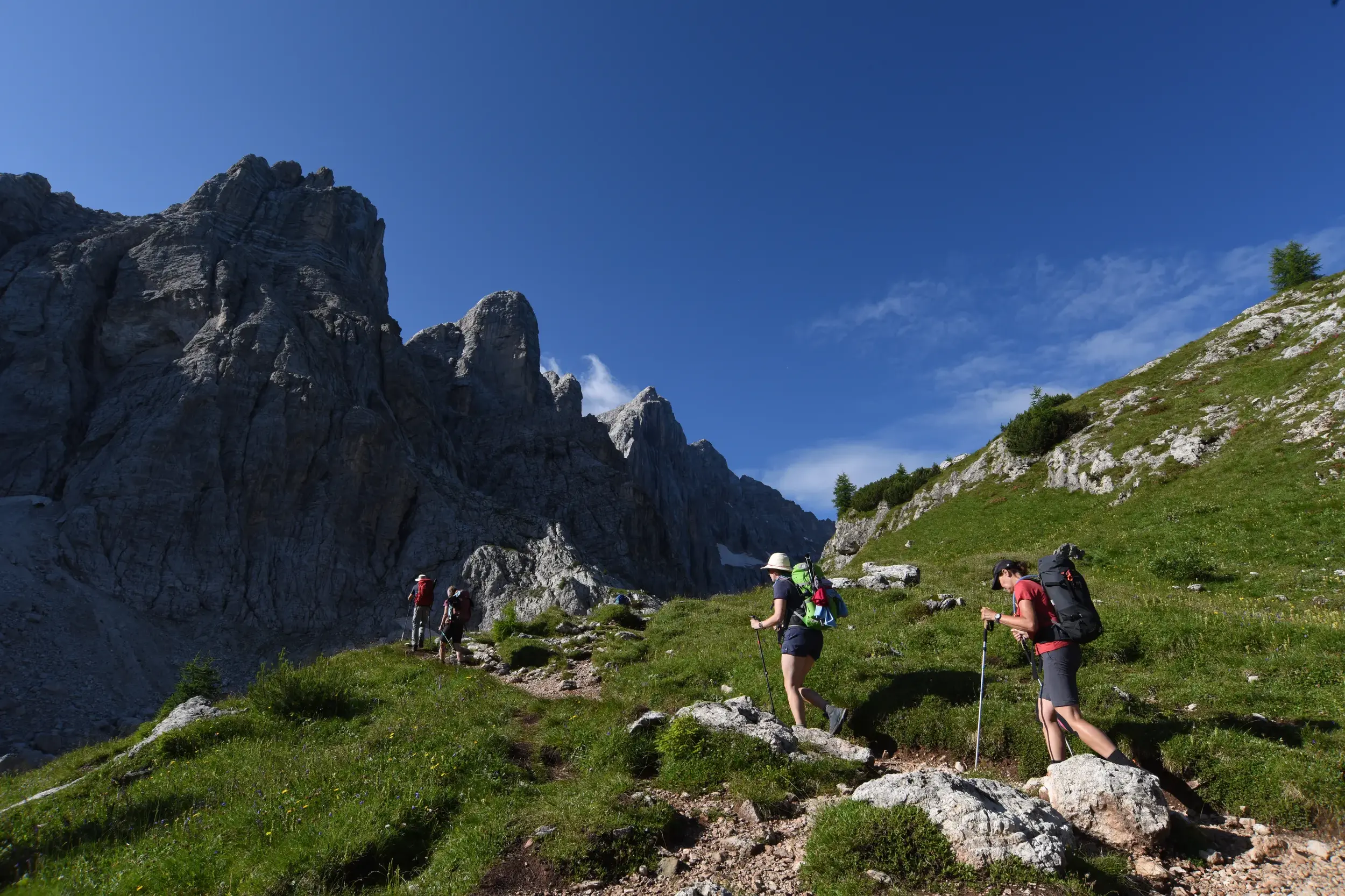 Eine Wandergruppe beim Trekking auf dem Höhenweg Alta Via 1 in den Dolomiten, vorbei an steilen Felswänden.