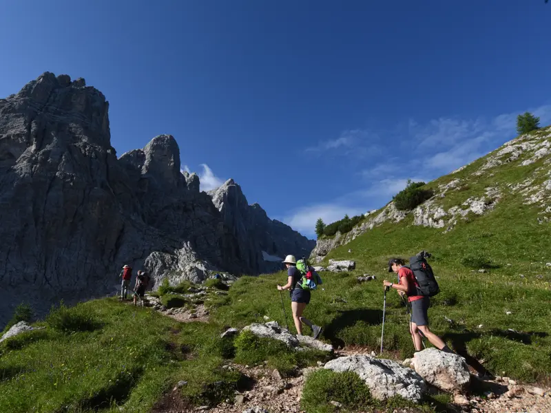Eine Wandergruppe beim Trekking auf dem Höhenweg Alta Via 1 in den Dolomiten, vorbei an steilen Felswänden.