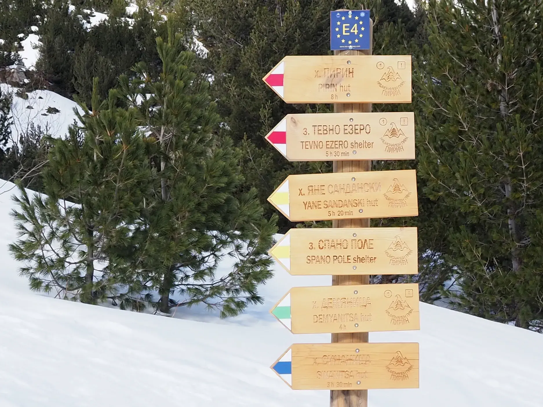 Hölzerner Wegweiser für Schneeschuhwanderungen im tiefen Schnee des bulgarischen Pirin-Gebirge auf dem E4-Wanderweg.