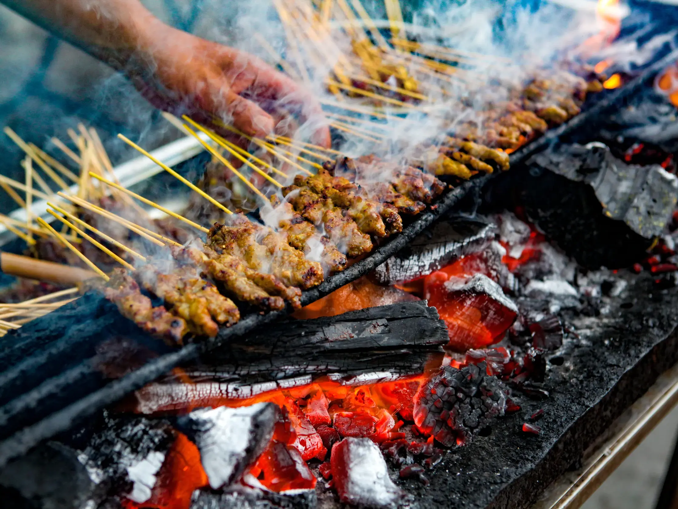 Brutzelnde Satay-Spieße werden von Hand über glühender Holzkohle auf einem Streetfood-Markt in Penang, Malaysia, gewendet.